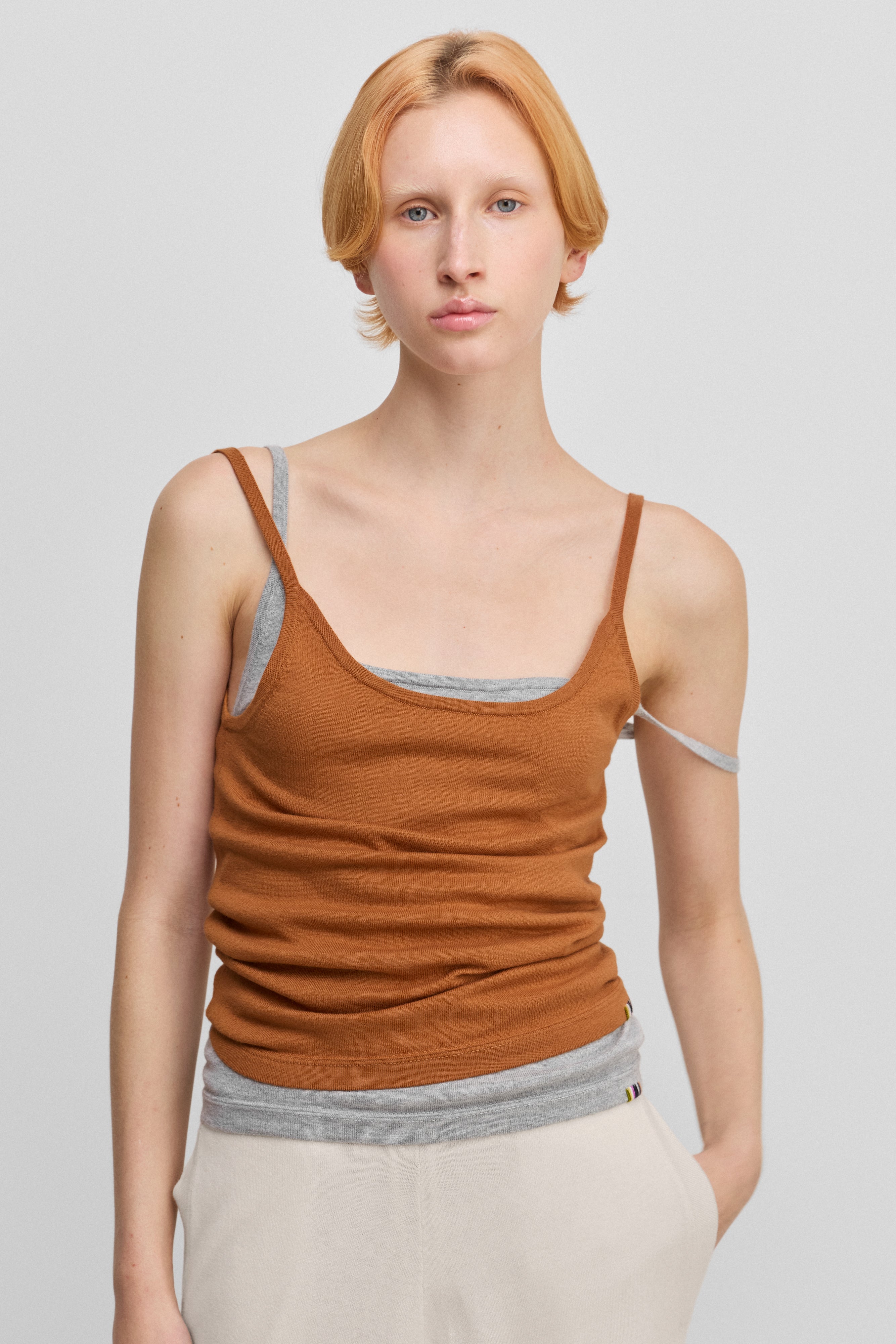 woman wearing an orange cotton cashmere strap top with a round neckline, worn over the same top in grey.