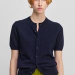 woman wearing a navy blue short-sleeved cashmere cardigan with eight corozo buttons and a crew neck.