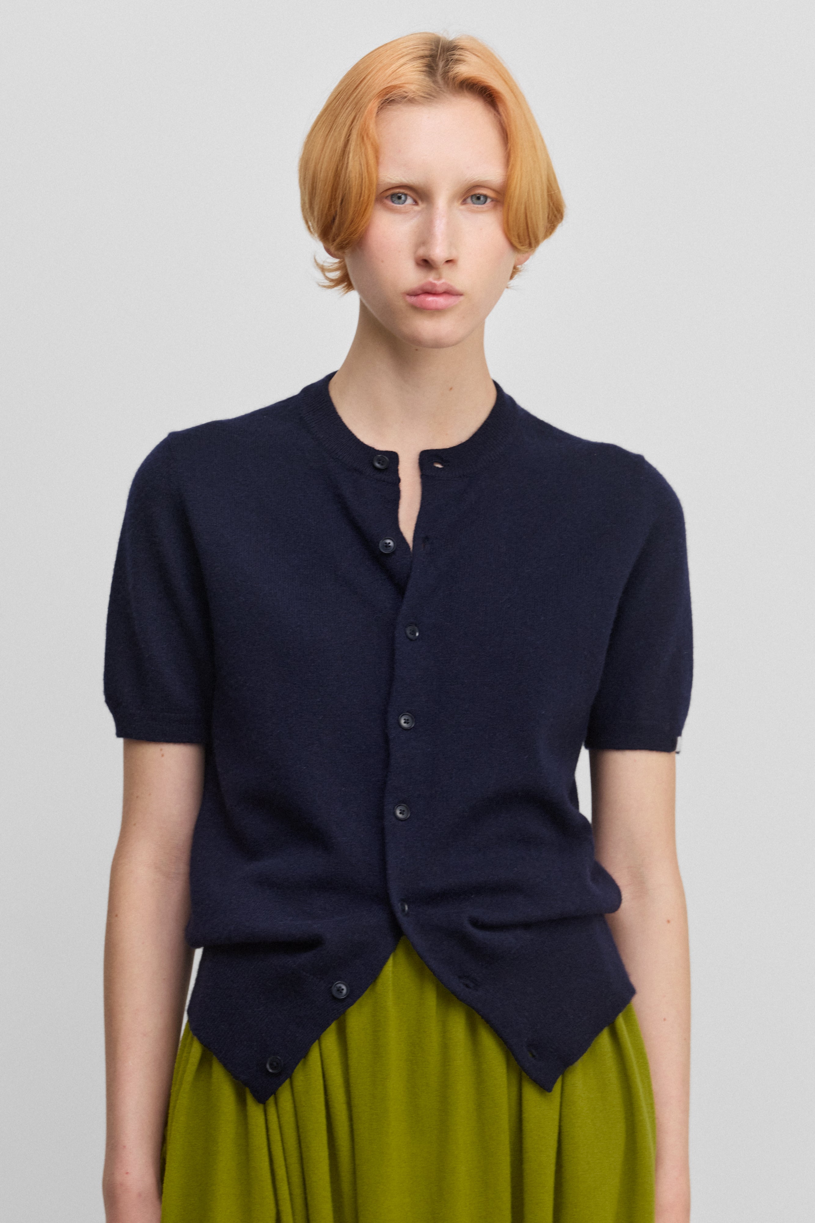 woman wearing a navy blue short-sleeved cashmere cardigan with eight corozo buttons and a crew neck.