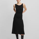 woman wearing a black sleeveless wool cashmere a-line dress in midi length with a boat neckline.