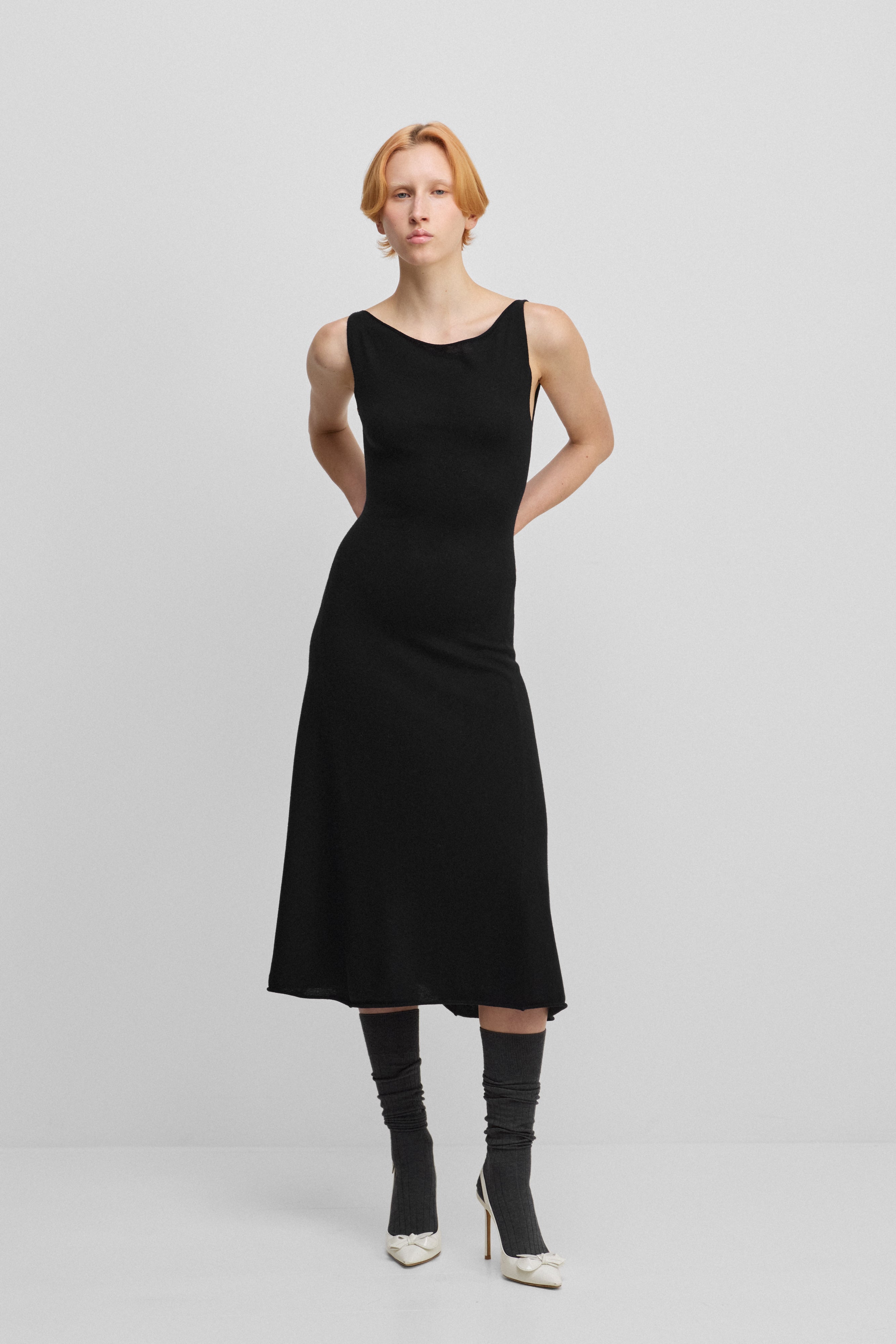 woman wearing a black sleeveless wool cashmere a-line dress in midi length with a boat neckline.