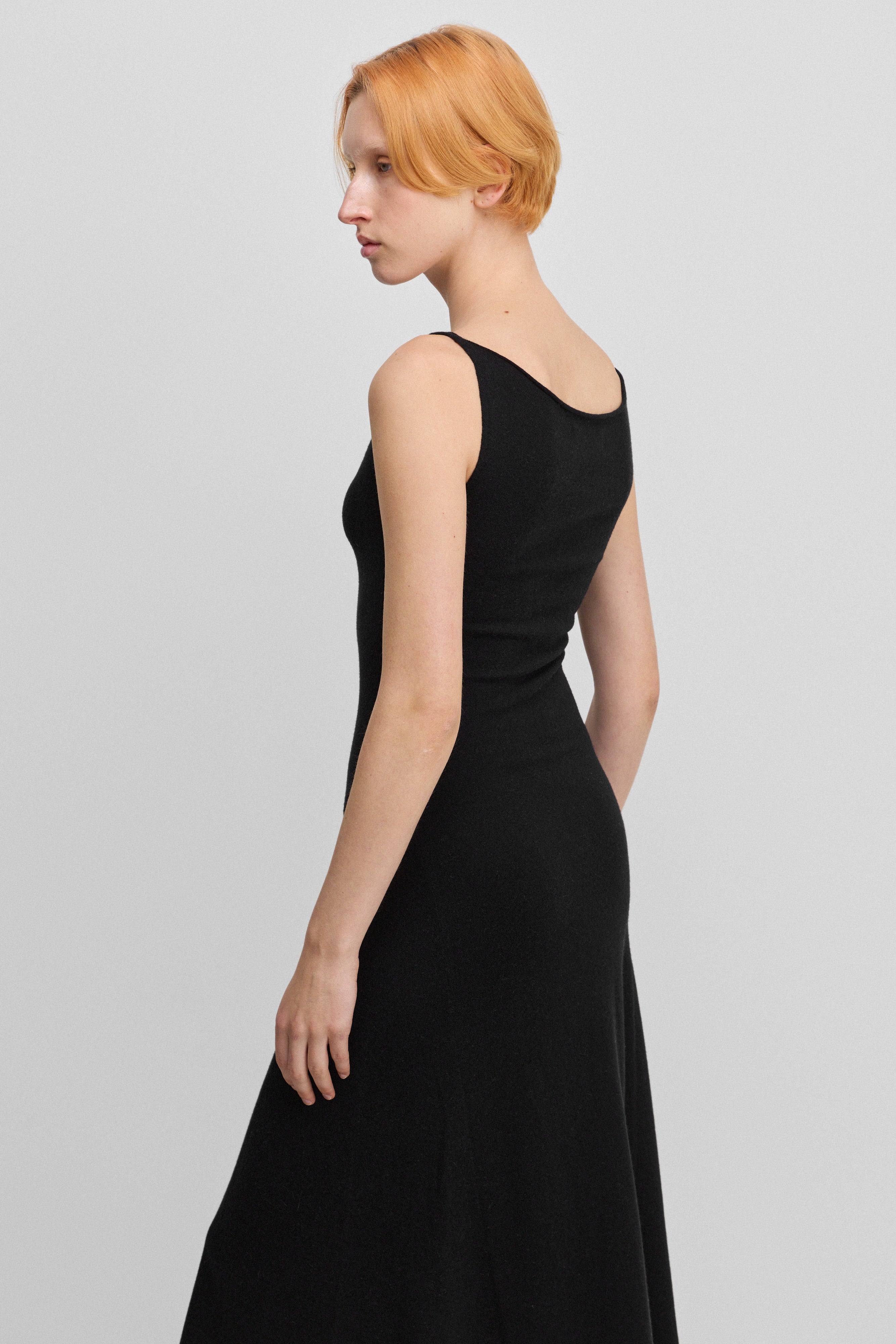 woman wearing a black sleeveless wool cashmere a-line dress, shown from the back.