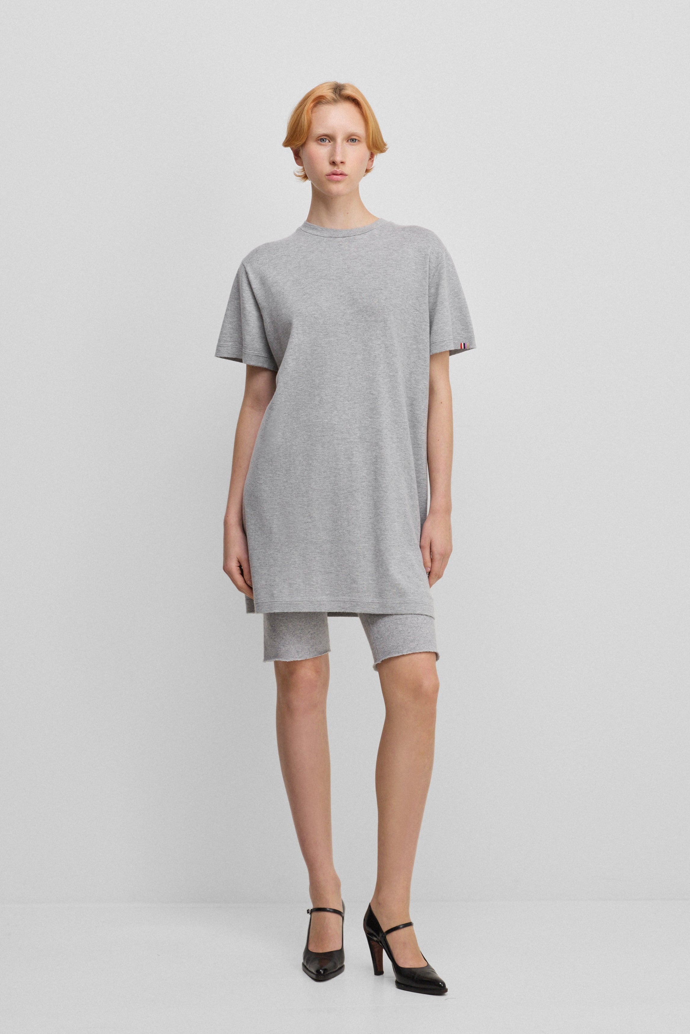 woman wearing a light grey cotton-cashmere mini t-shirt dress, styled with grey biker shorts.