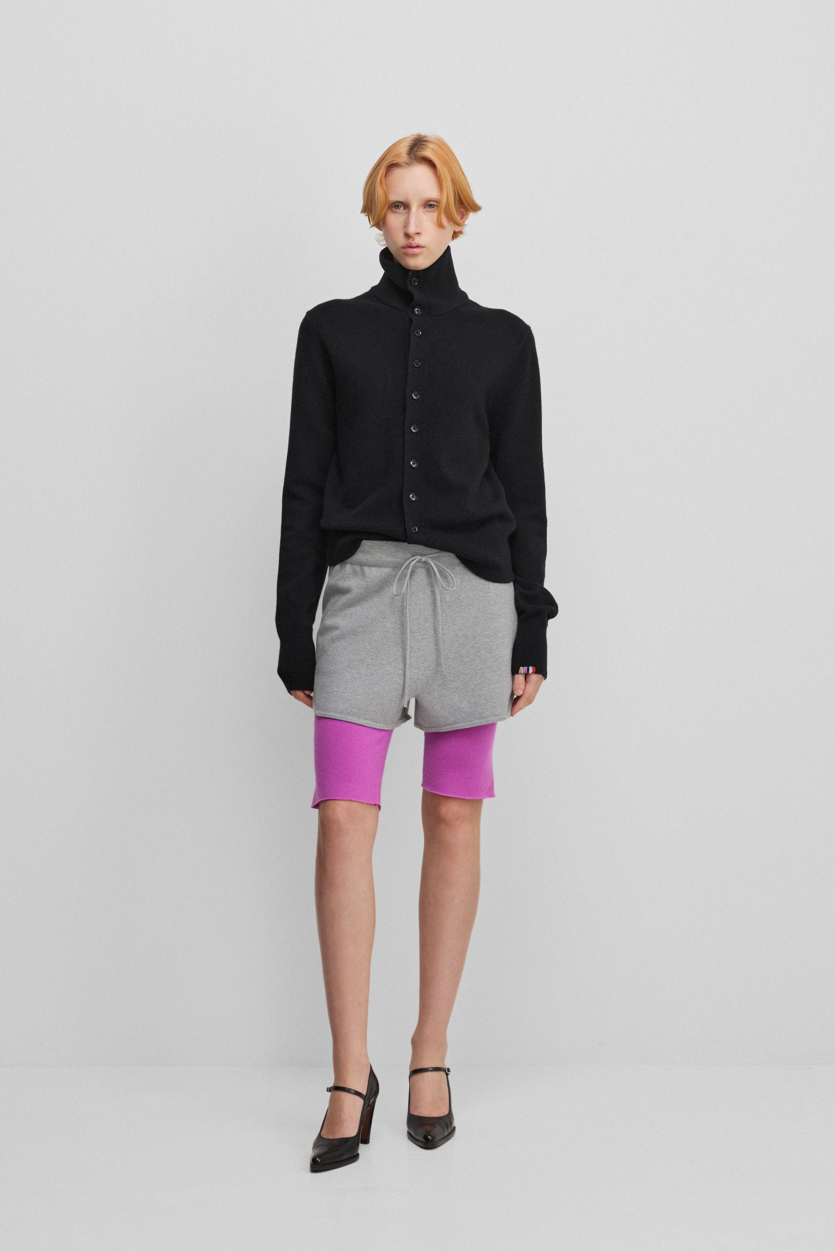 woman wearing a black cashmere button-up cardigan with a rib-knitted collar, styled with grey shorts.