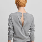 woman wearing a grey cotton cashmere long-sleeved top with a half button closure on the back, shown from the back.