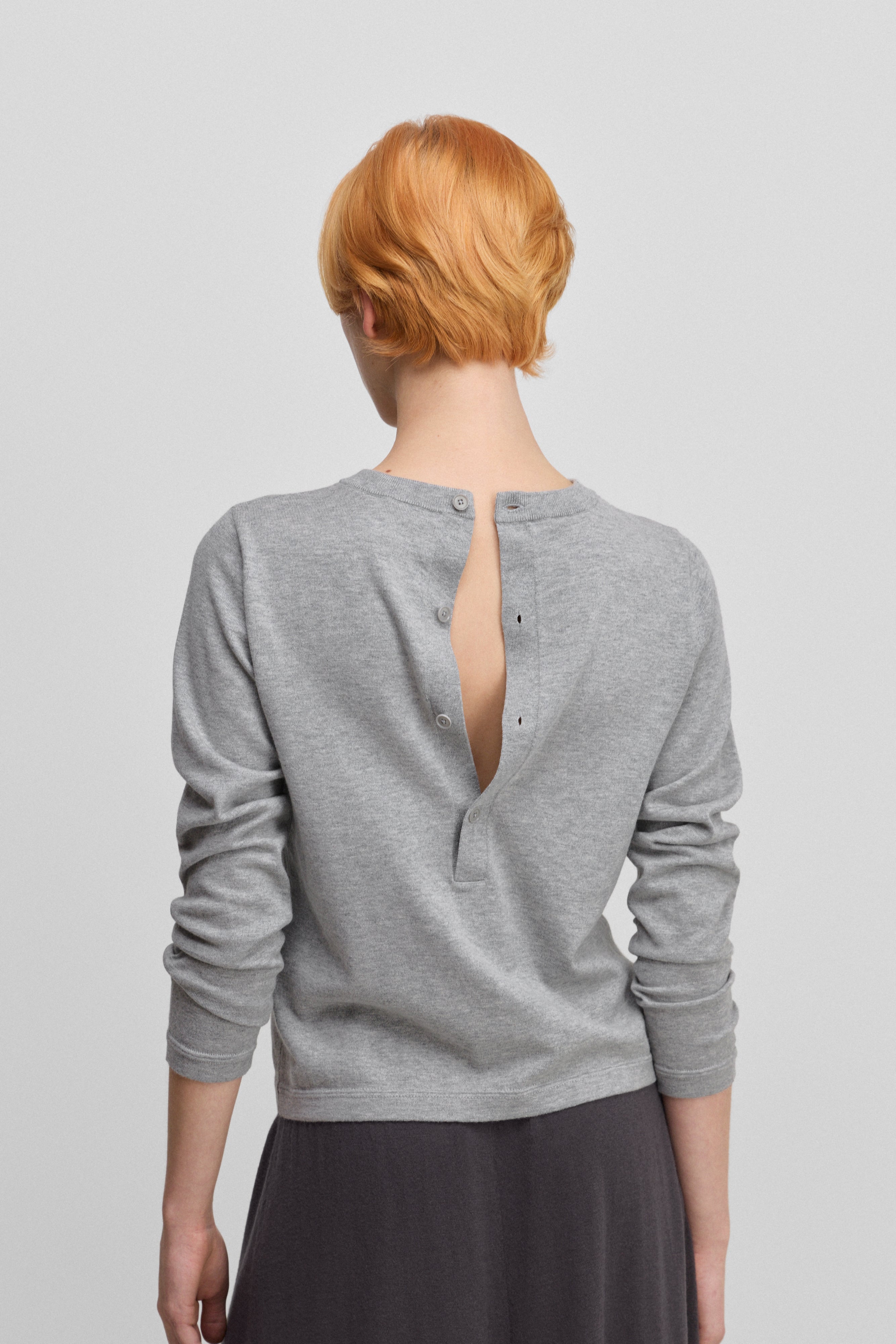 woman wearing a grey cotton cashmere long-sleeved top with a half button closure on the back, shown from the back.