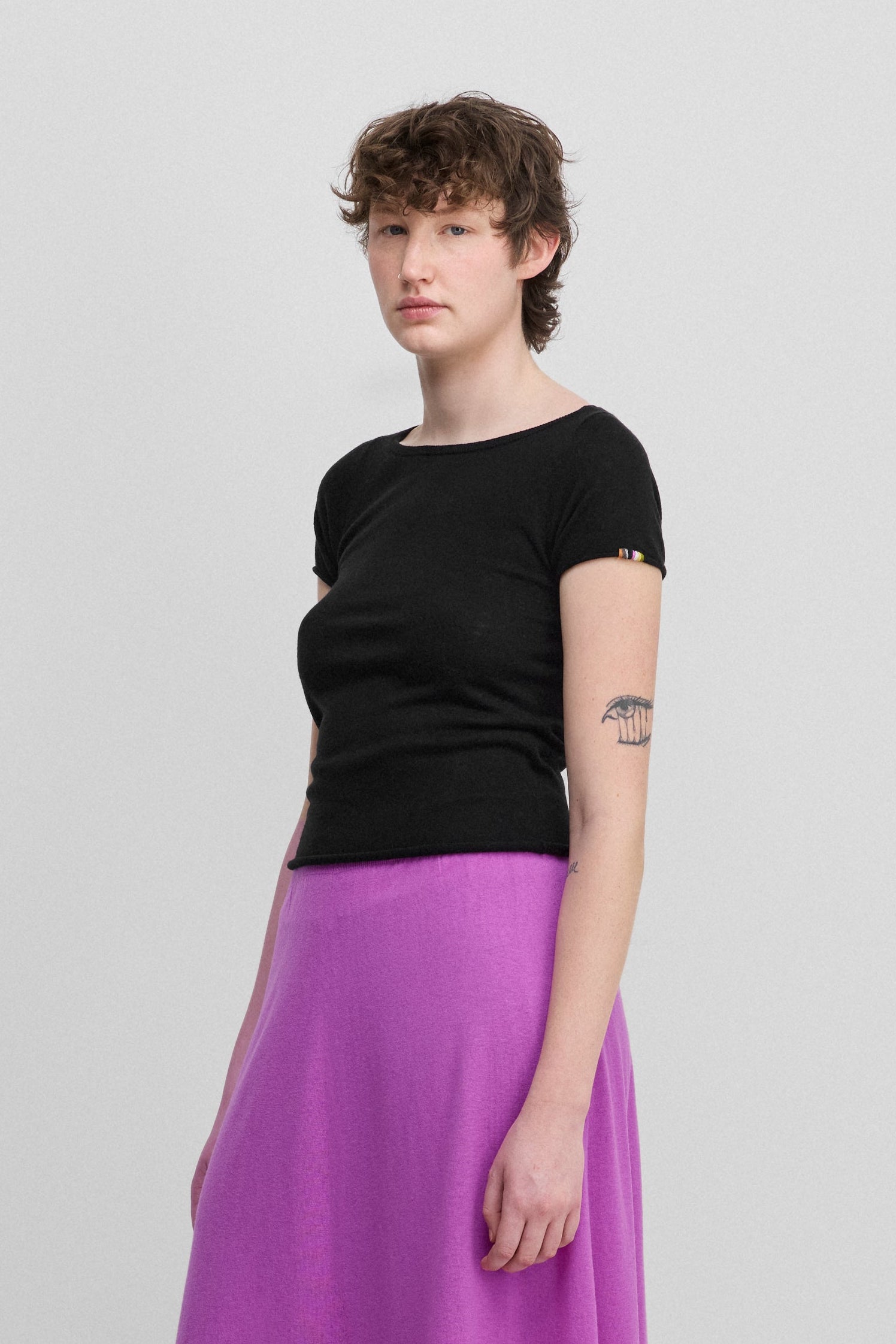 woman wearing a black fitted wool cashmere t-shirt with a boat neck, styled with a pink skirt.