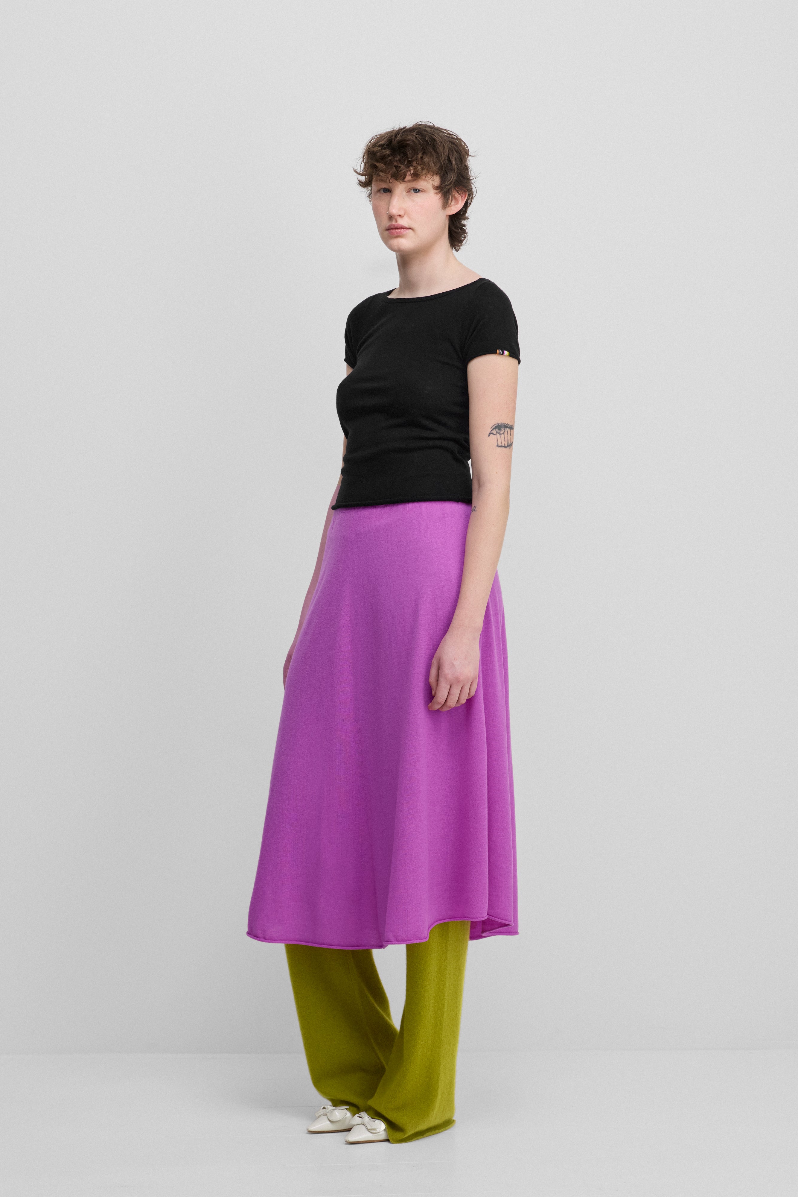 woman wearing a black fitted wool cashmere t-shirt with a boat neck, styled with a pink skirt.
