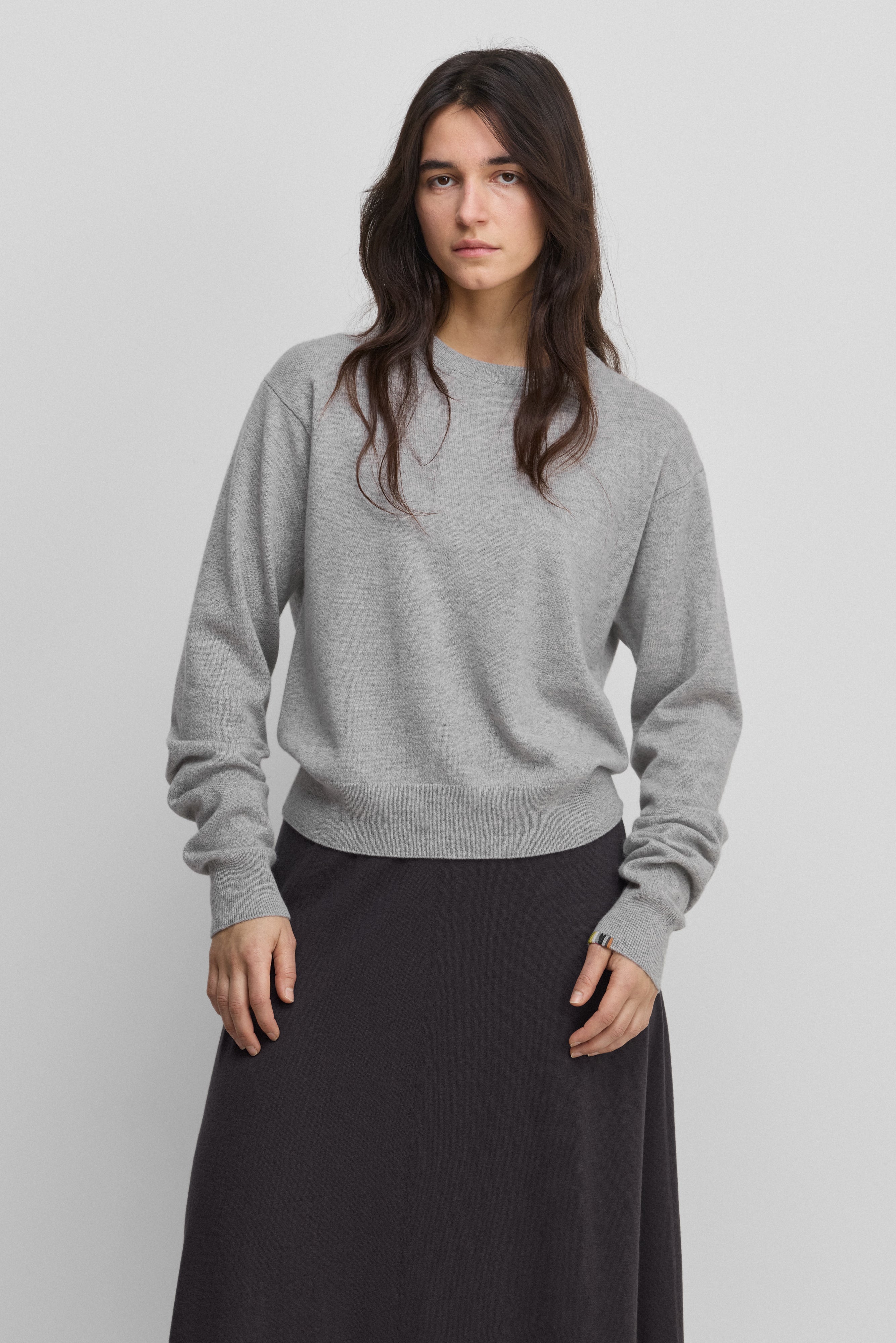 woman wearing a light grey cashmere crew-neck sweater with ribbed hem, cuffs, neckline.