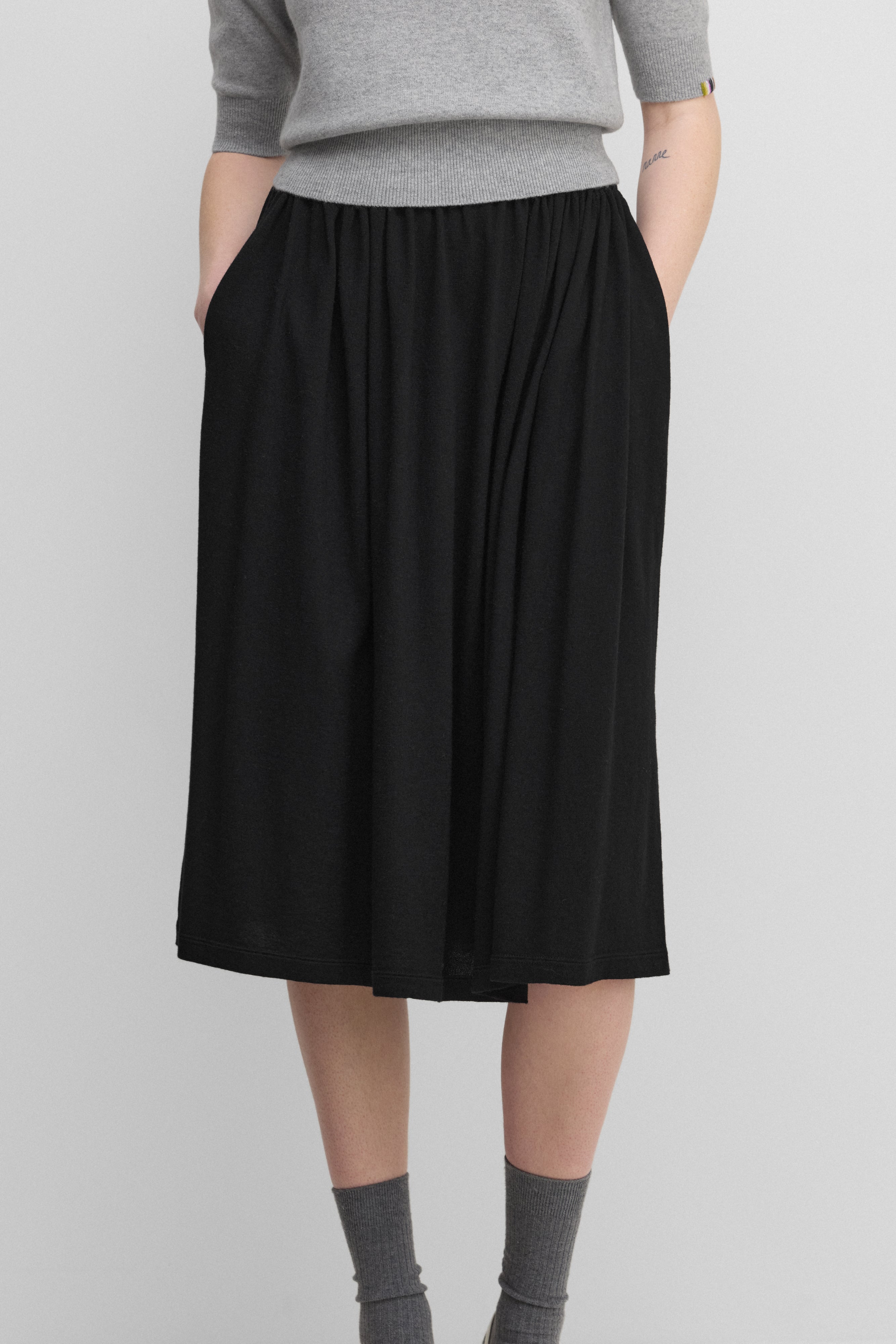 woman wearing a black cotton cashmere midi skirt with an elasticated waistband and two side pockets.