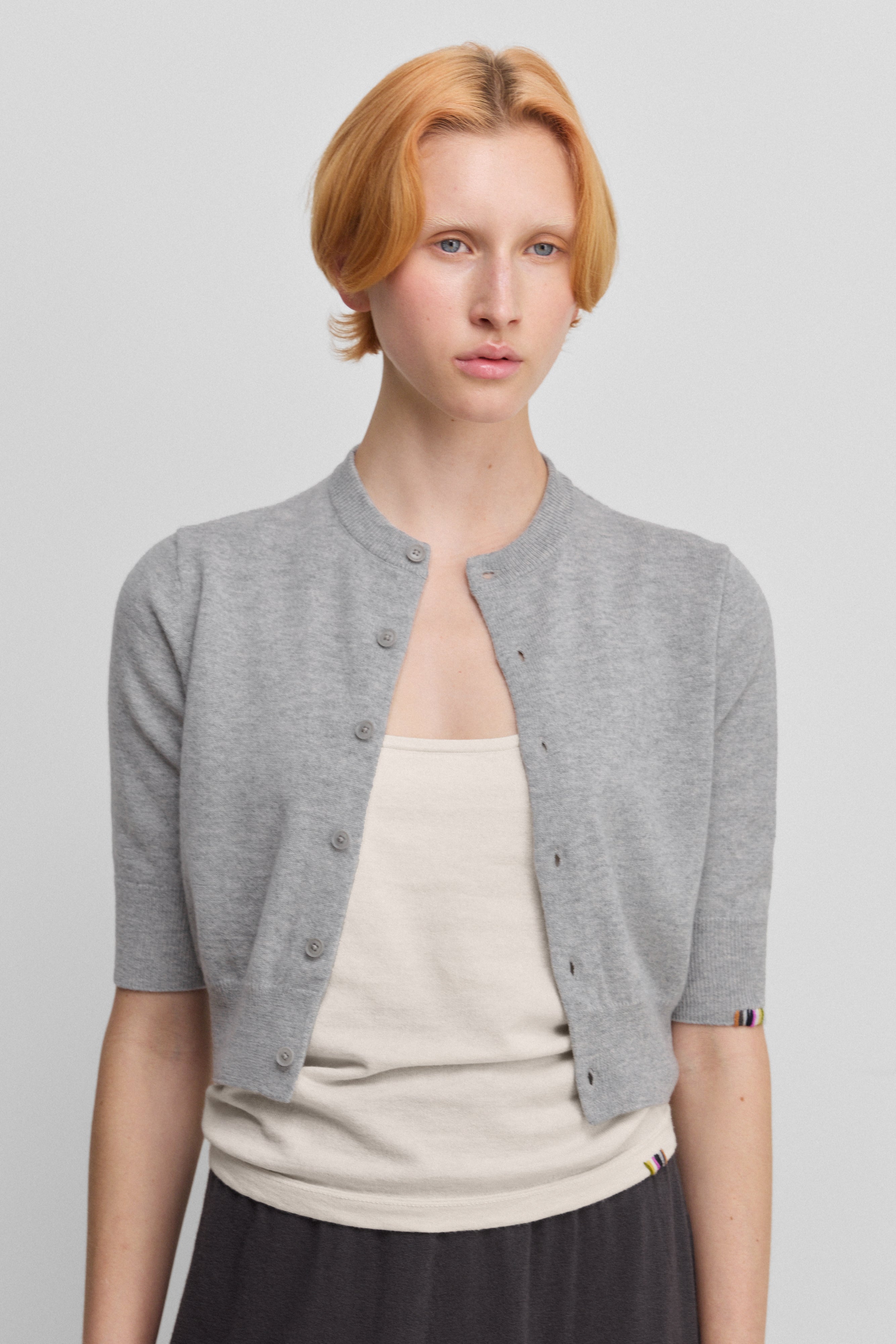 woman wearing an orange cropped button-up cardigan with elbow-length sleeves, worn over a white top.