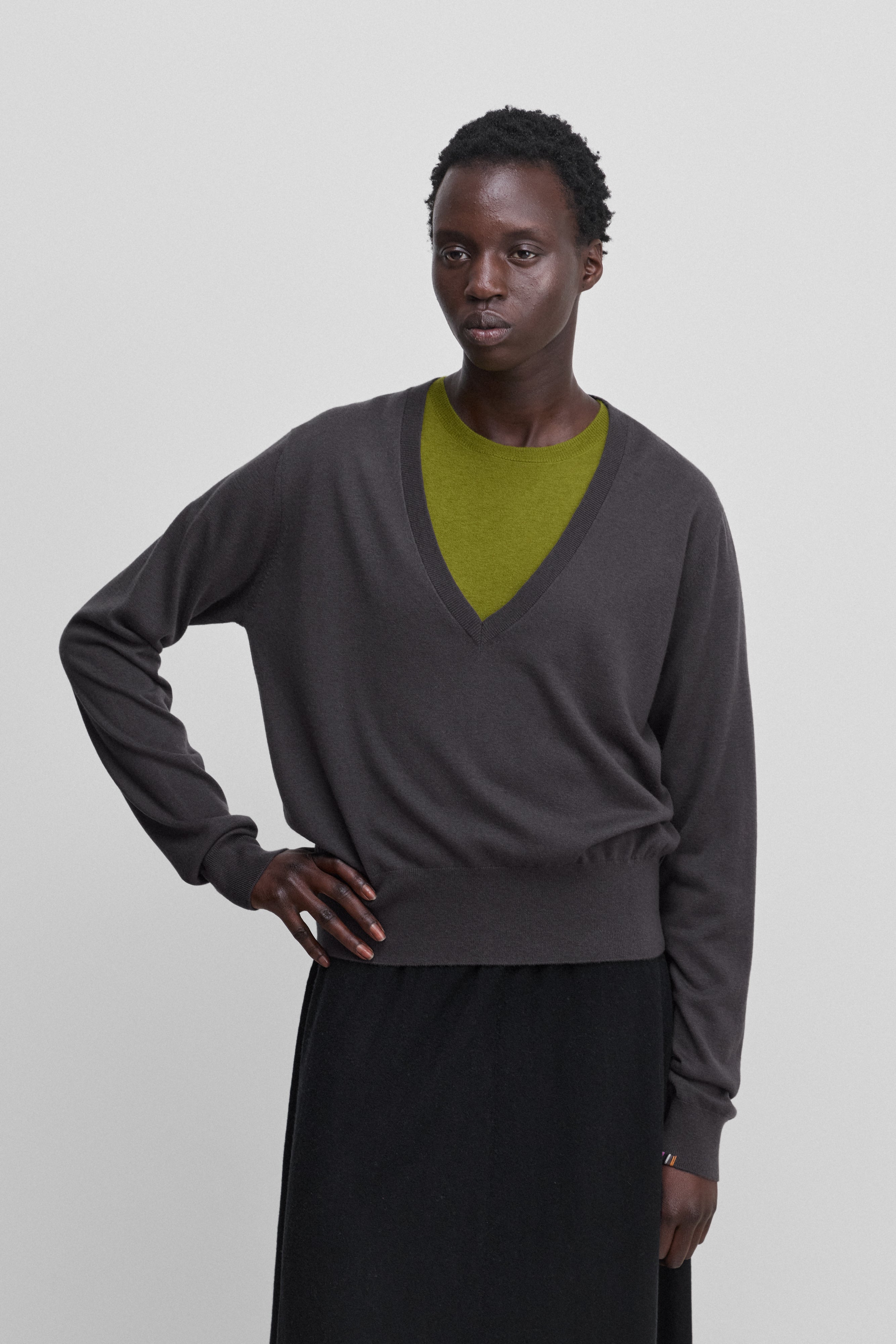 woman wearing a dark grey wool cashmere v-neck sweater with ribbed hem and cuffs, worn over a green t-shirt.