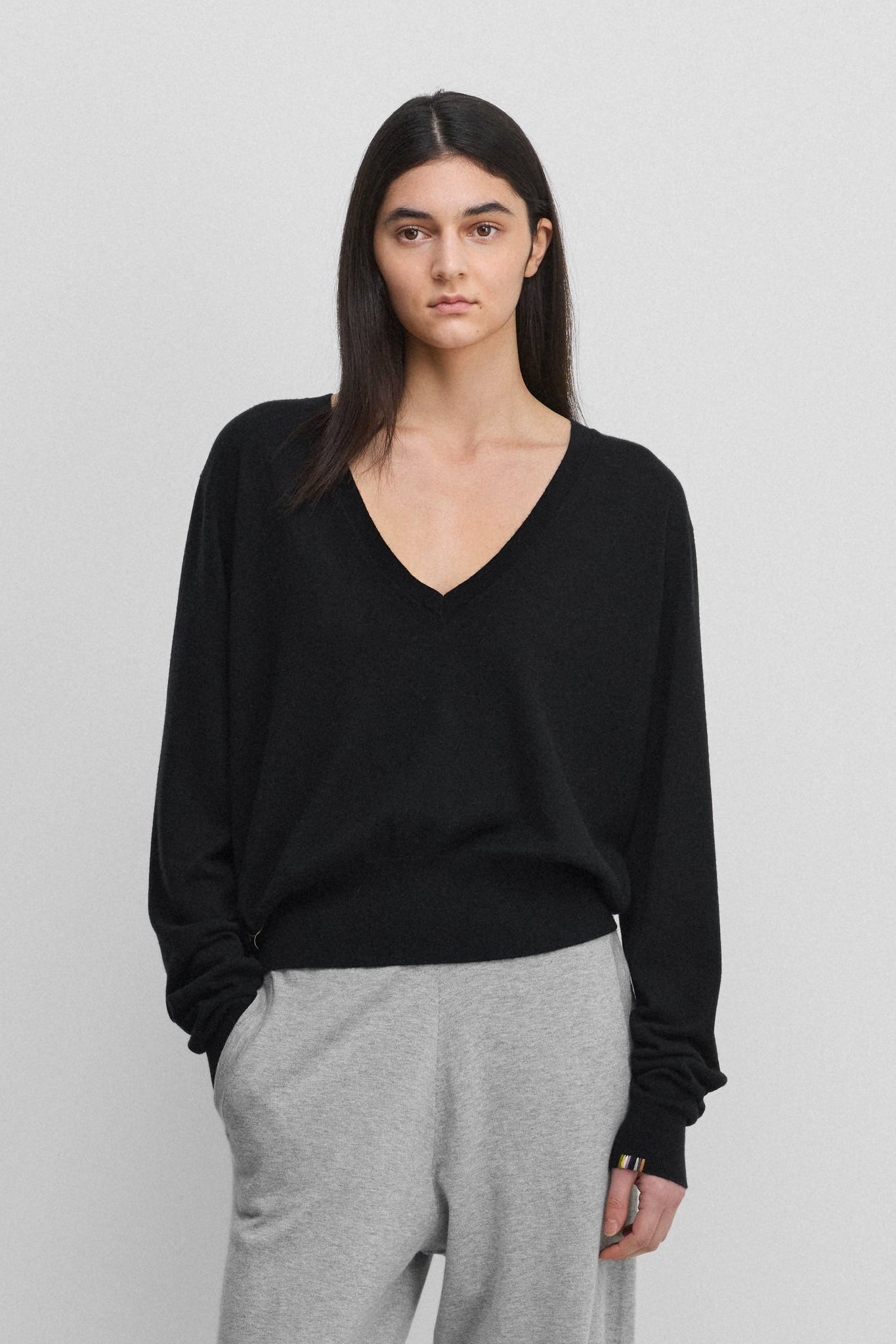 woman wearing a black wool cashmere v-neck sweater with a ribbed hem and cuffs, styled with grey pants.