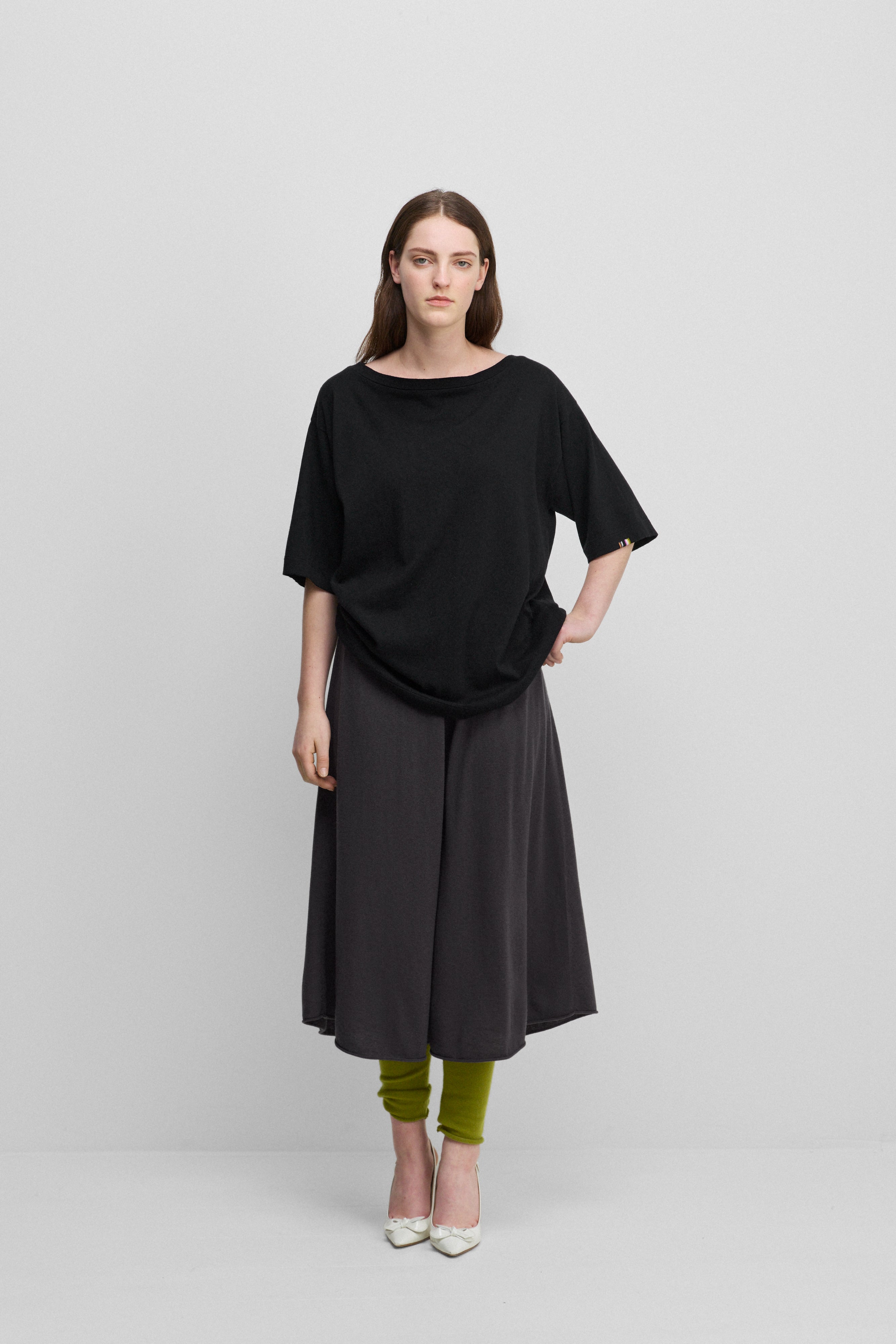 woman wearing an oversized black cotton cashmere boat-neck t-shirt with elbow-length sleeves, styled with a skirt.