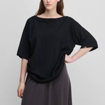 woman wearing an oversized black cotton cashmere t-shirt with a boat neck and elbow-length sleeves.