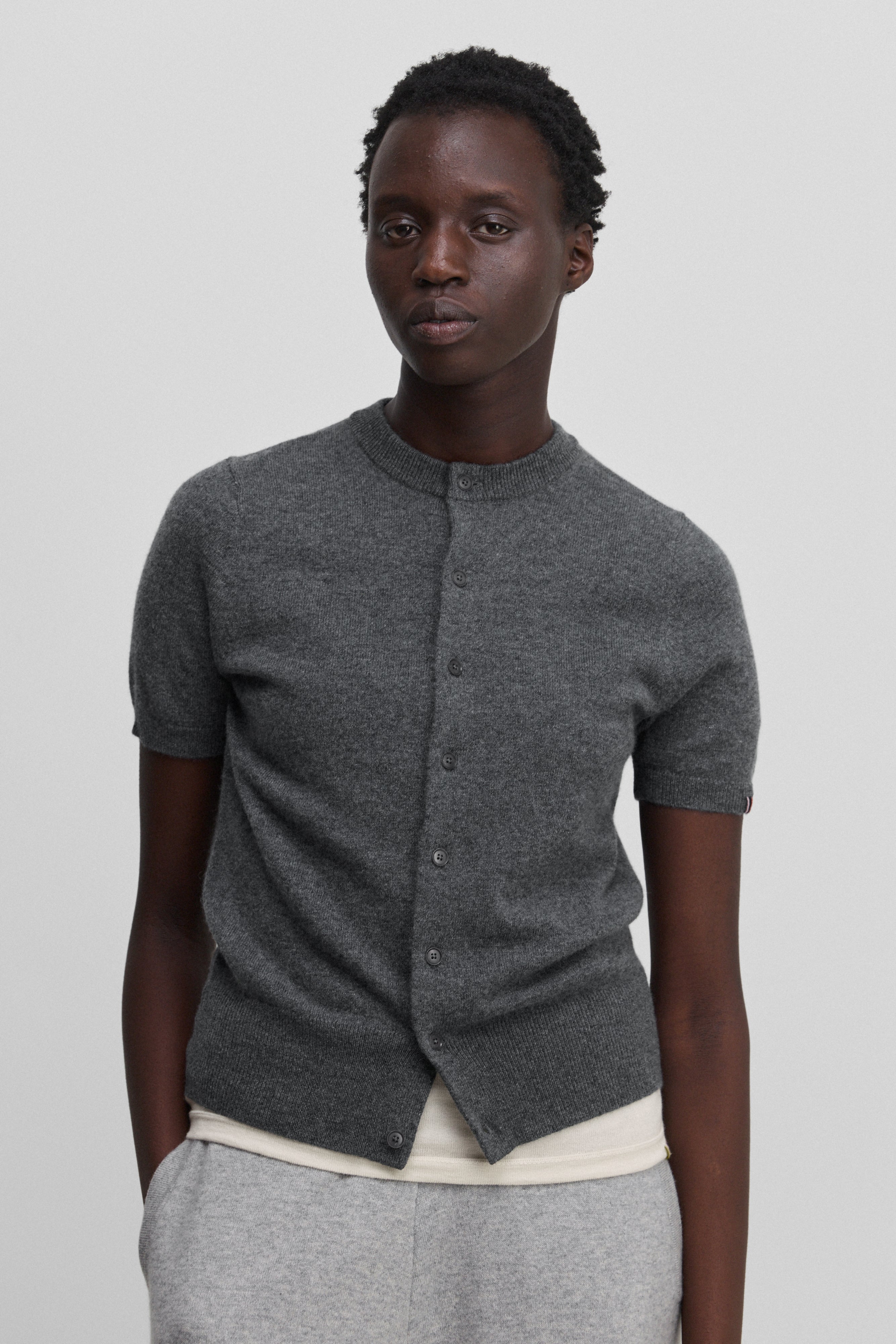 woman wearing a dark grey short-sleeved cashmere button-up cardigan with rib-knitted hem and cuffs.