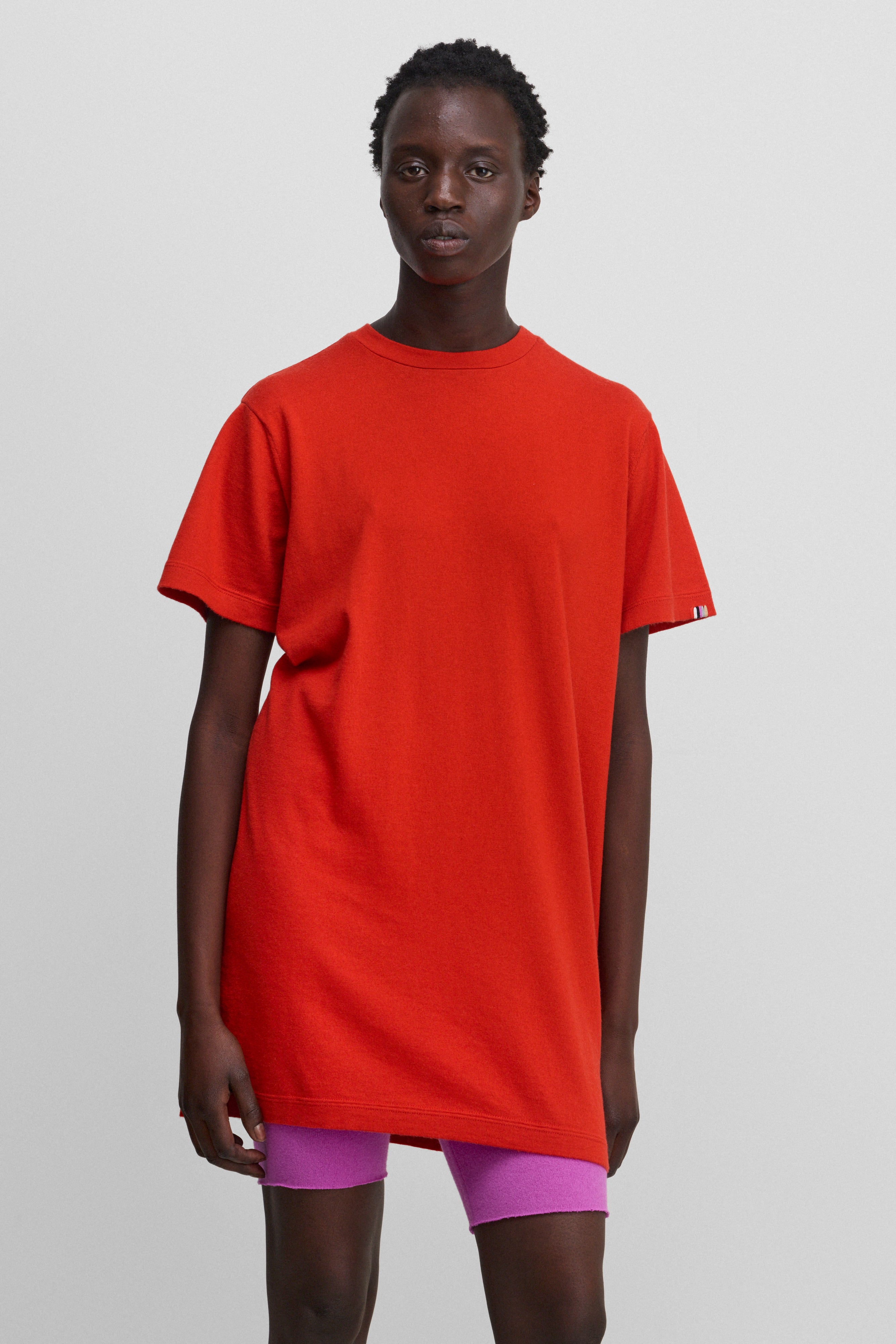 woman wearing a bright red cotton-cashmere mini t-shirt dress, styled with pink biker shorts.