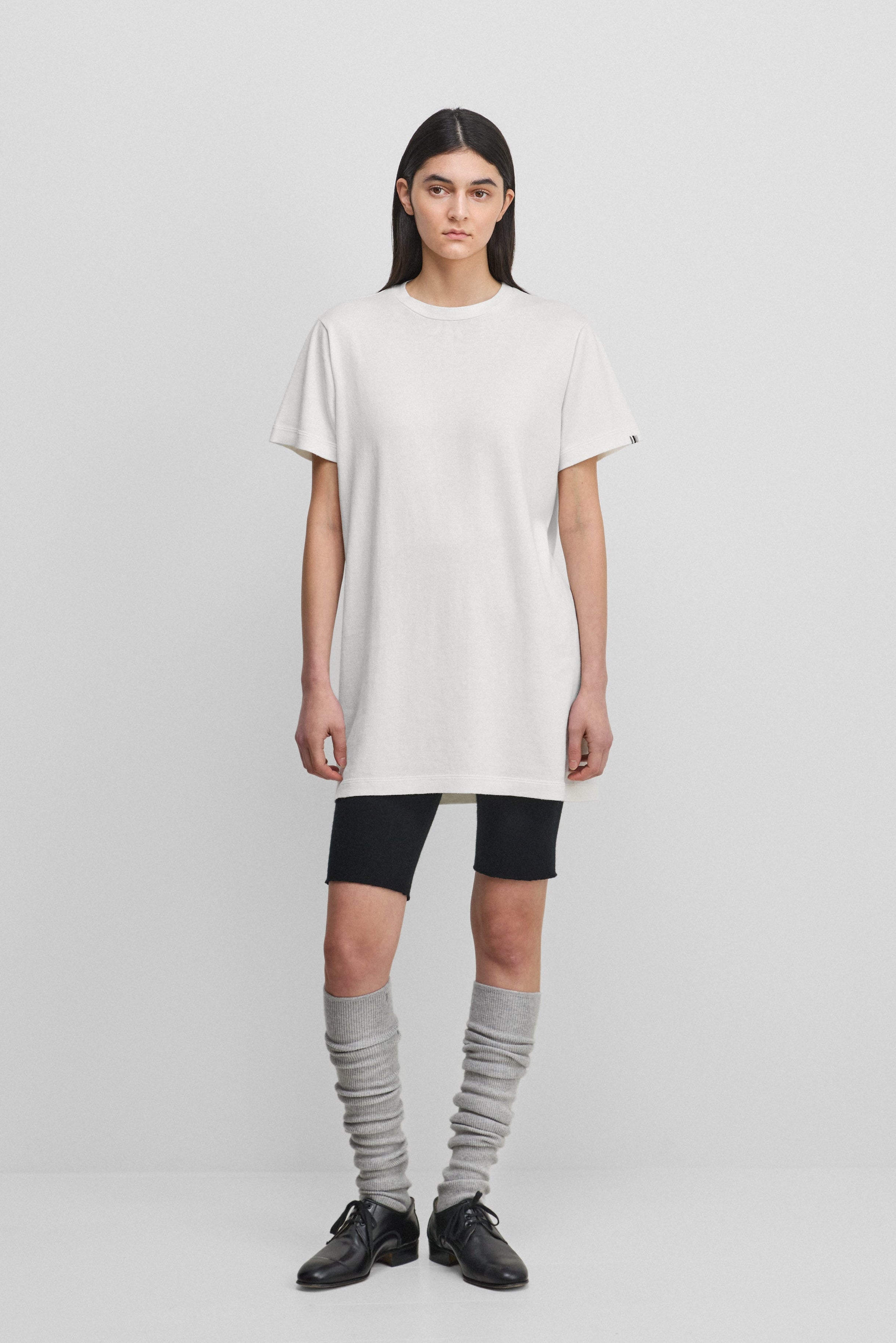 woman wearing a white cotton-cashmere mini t-shirt dress, styled with black biker shorts.
