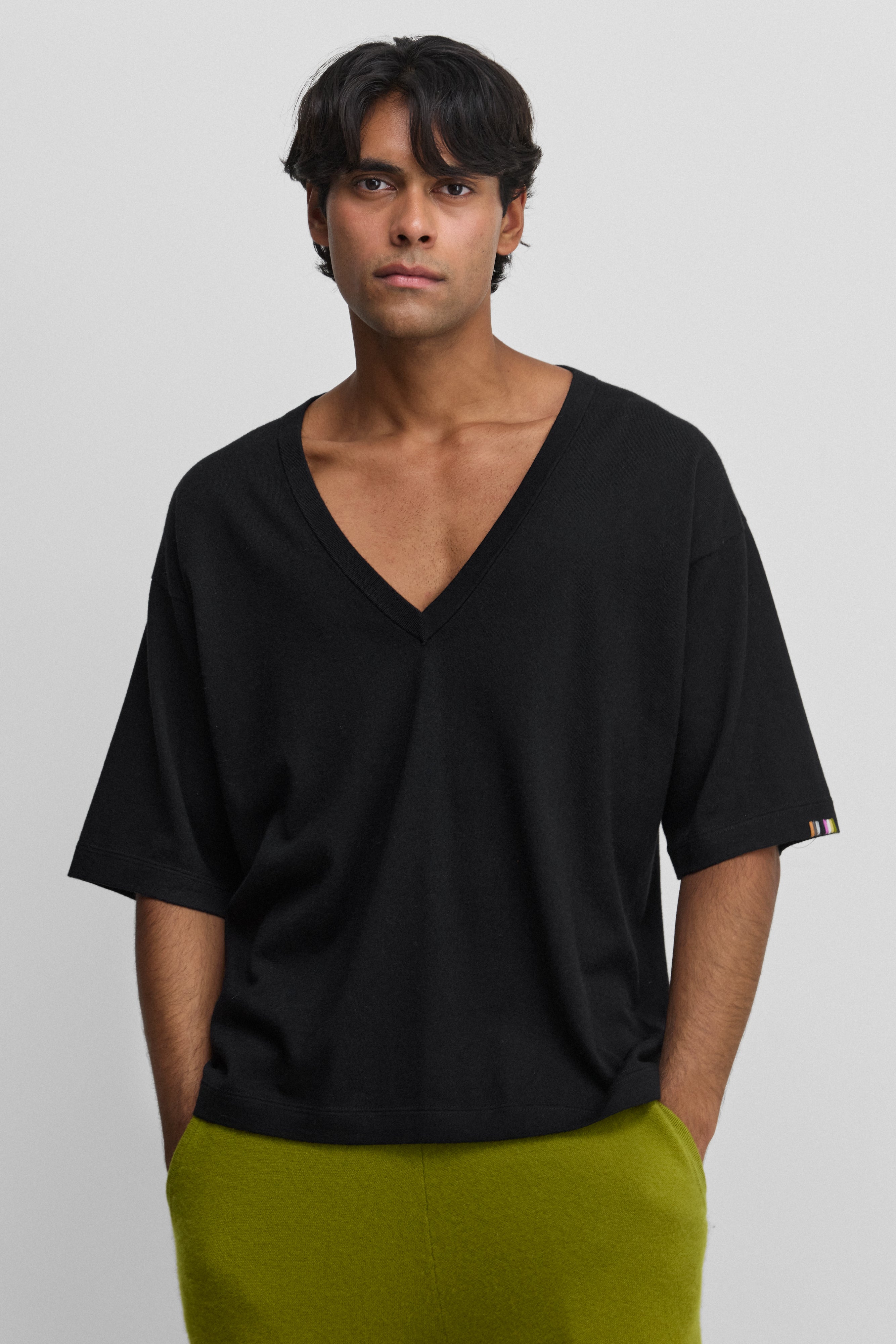 man wearing a loose-fit black cotton cashmere t-shirt with a deep v-neck and elbow-length sleeves.