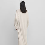 woman wearing a white floor-length long-sleeved dress in cotton cashmere, shown from behind.