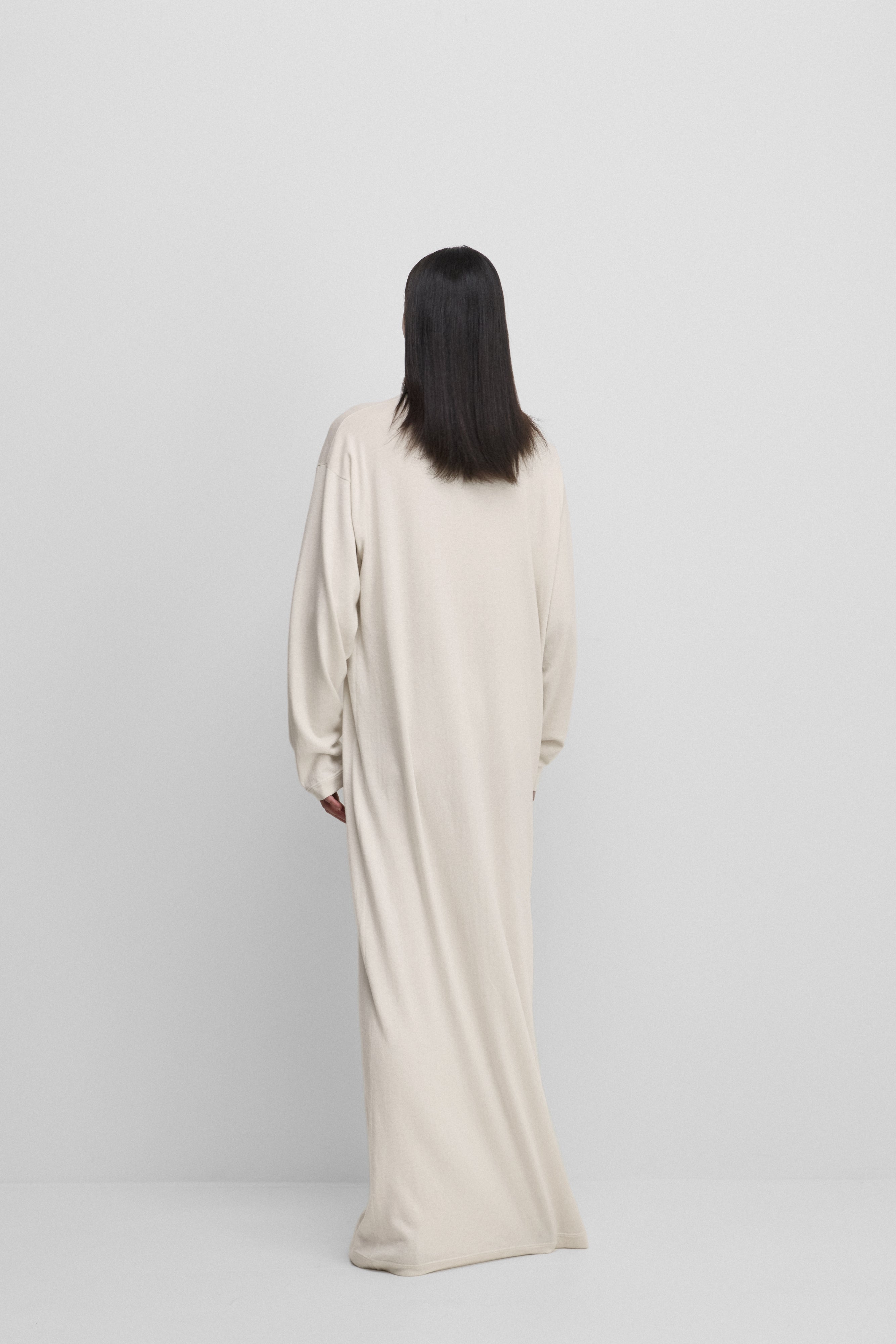 woman wearing a white floor-length long-sleeved dress in cotton cashmere, shown from behind.