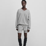 woman wearing a light grey relaxed-fit cashmere v-neck sweater with ribbed trims, styled with grey shorts.