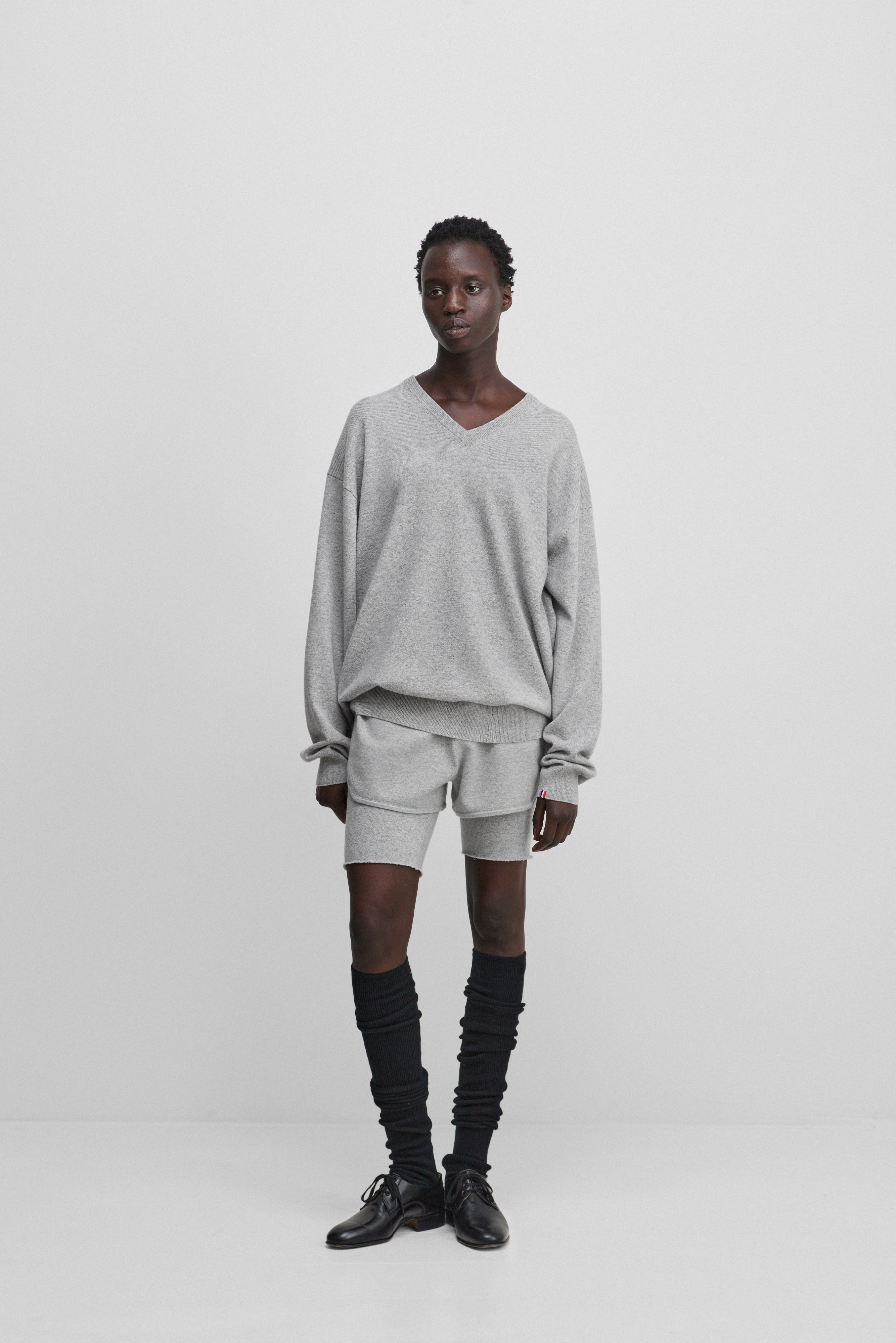 woman wearing a light grey relaxed-fit cashmere v-neck sweater with ribbed trims, styled with grey shorts.