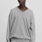 woman wearing a light grey relaxed-fit cashmere v-neck sweater with ribbed trims.
