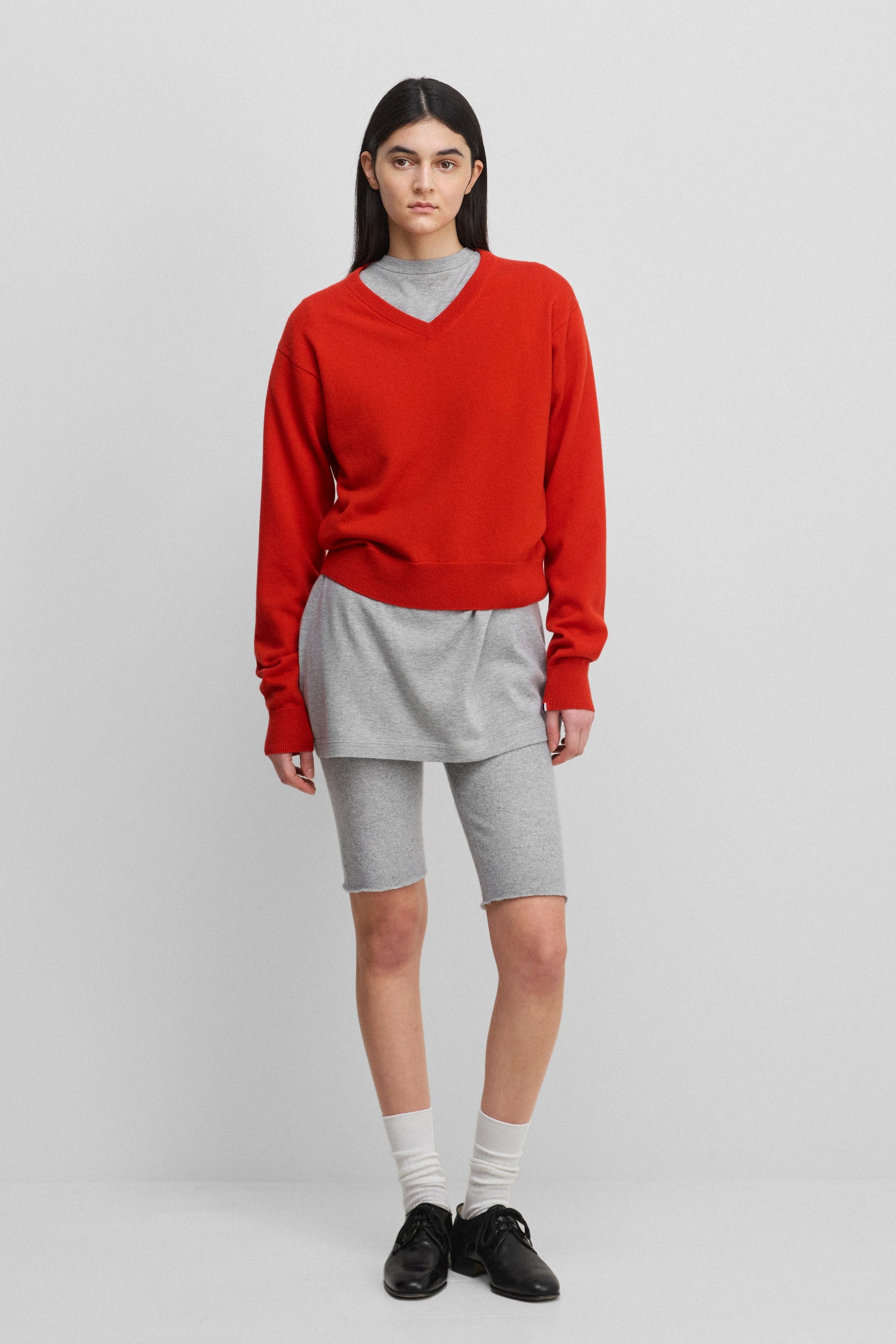 woman wearing a bright red classic-fit cashmere v-neck sweater, styled with grey biker shorts.