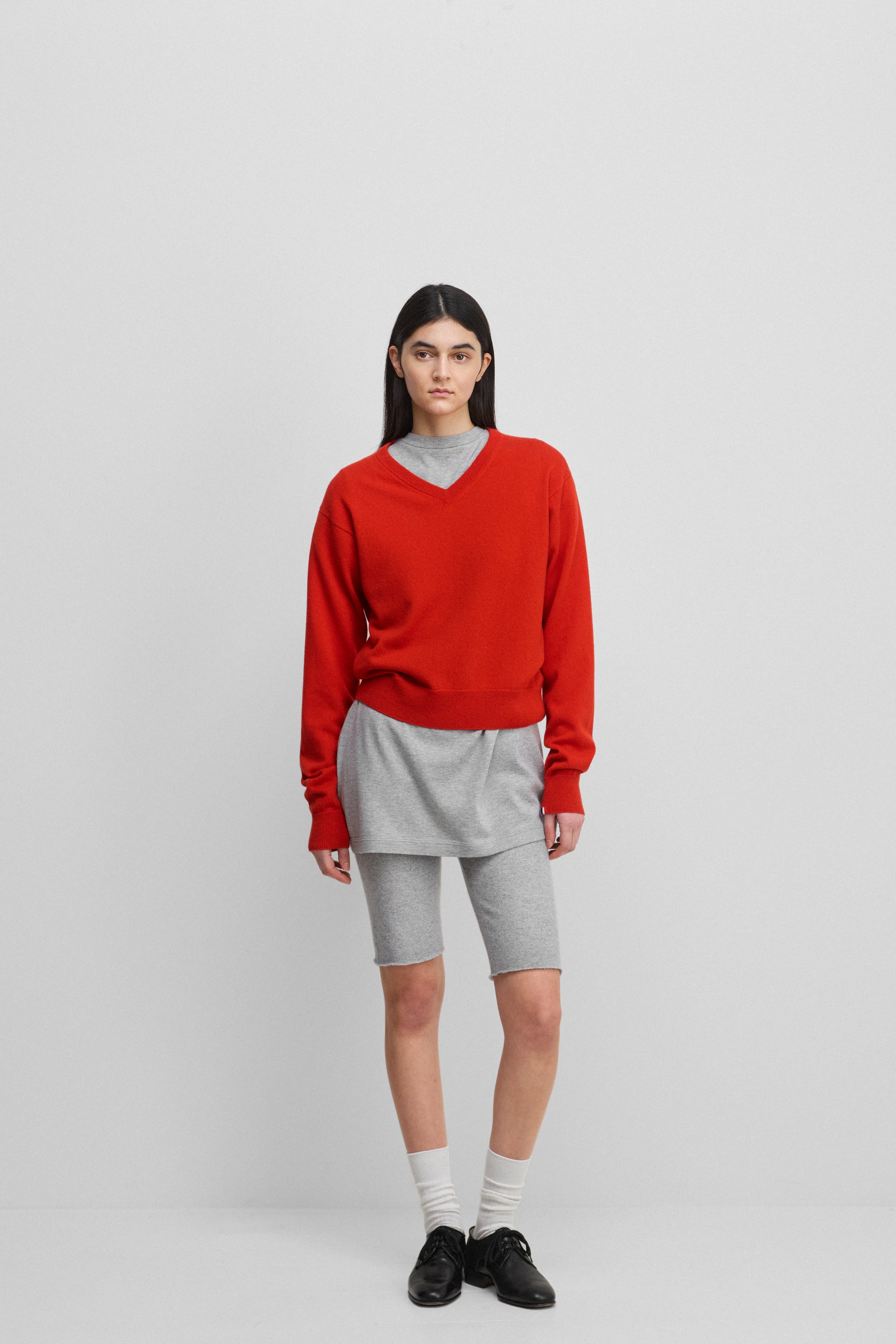 woman wearing a bright red classic-fit cashmere v-neck sweater, styled with grey biker shorts.