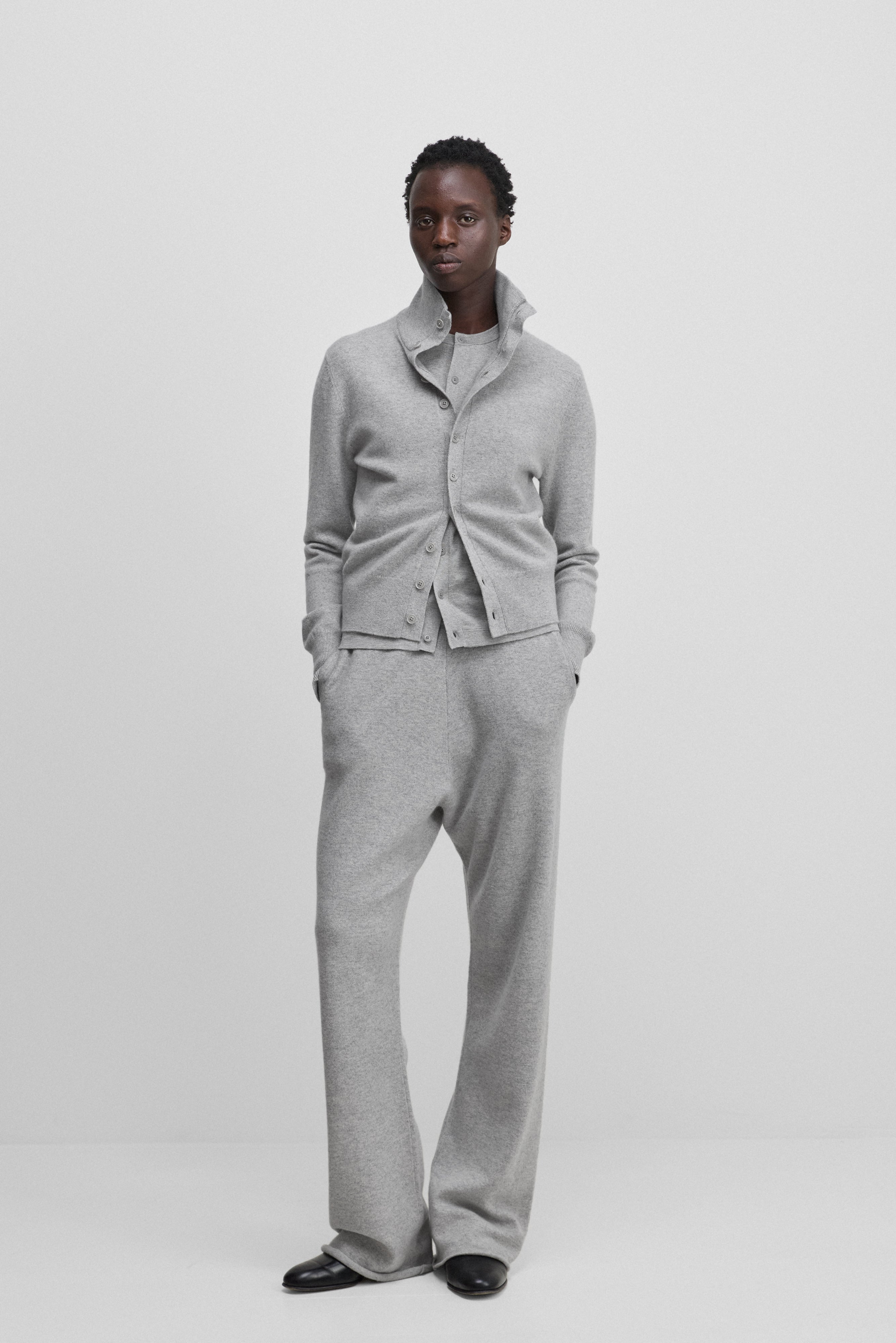 woman wearing a light grey cashmere button-up cardigan with a rib-knitted collar, styled with grey pants.