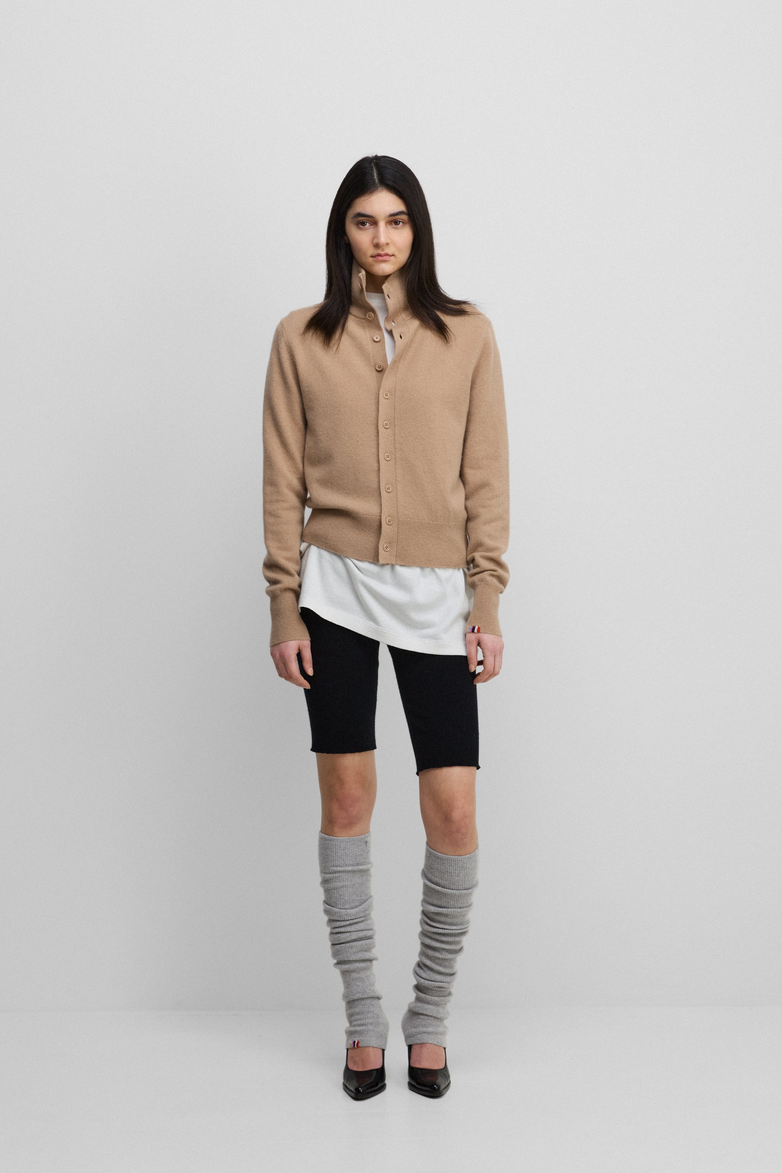 woman wearing a camel beige cashmere button-up cardigan with a rib-knitted collar, styled with black biker shorts.