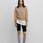woman wearing grey cashmere leg warmers, styled with black biker shorts, and a beige cardigan.