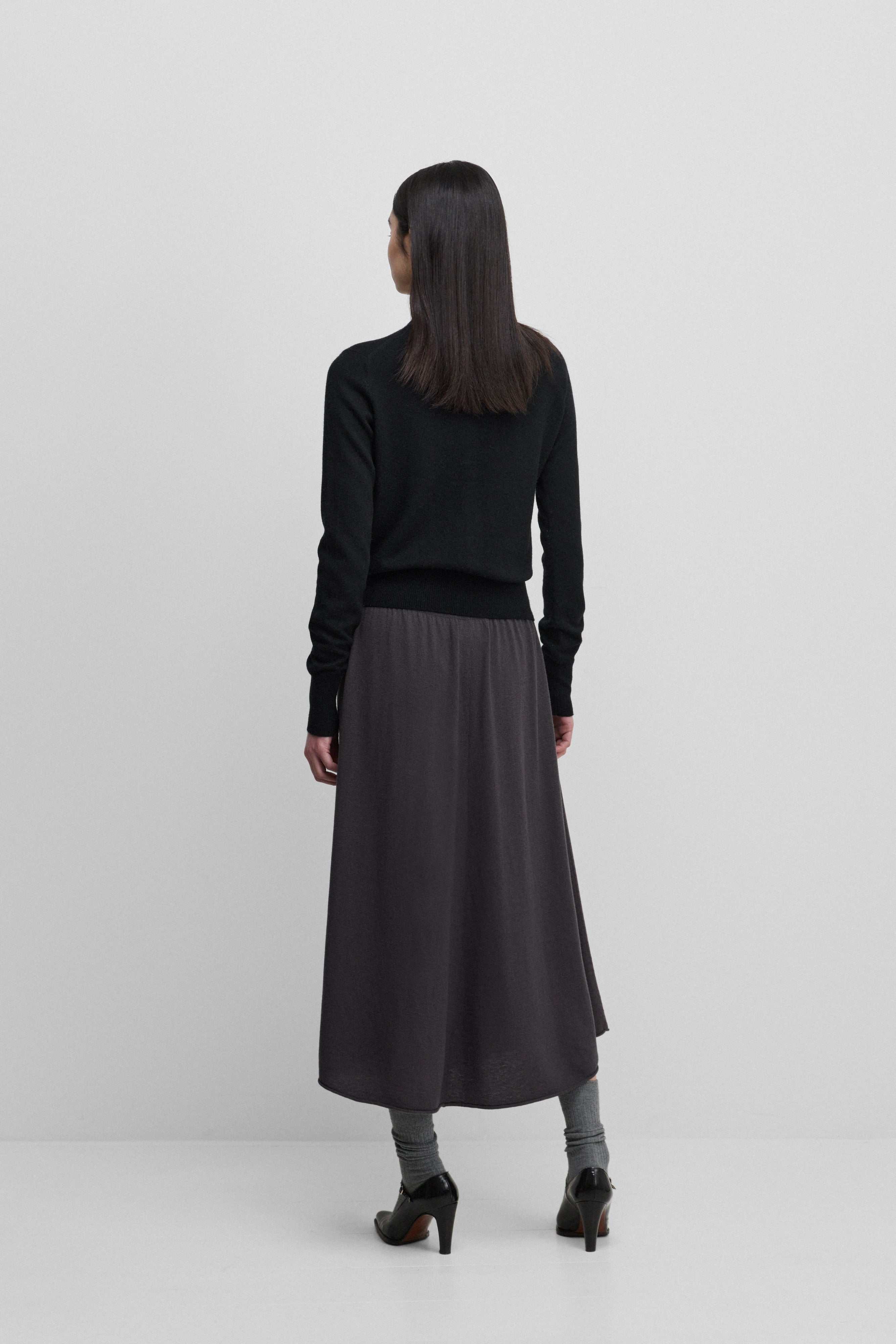 woman wearing a dark grey wool cashmere midi skirt, shown from the back.