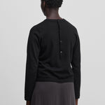 woman wearing a black cotton cashmere long-sleeved t-shirt with half button closure on the back, shown from the back.