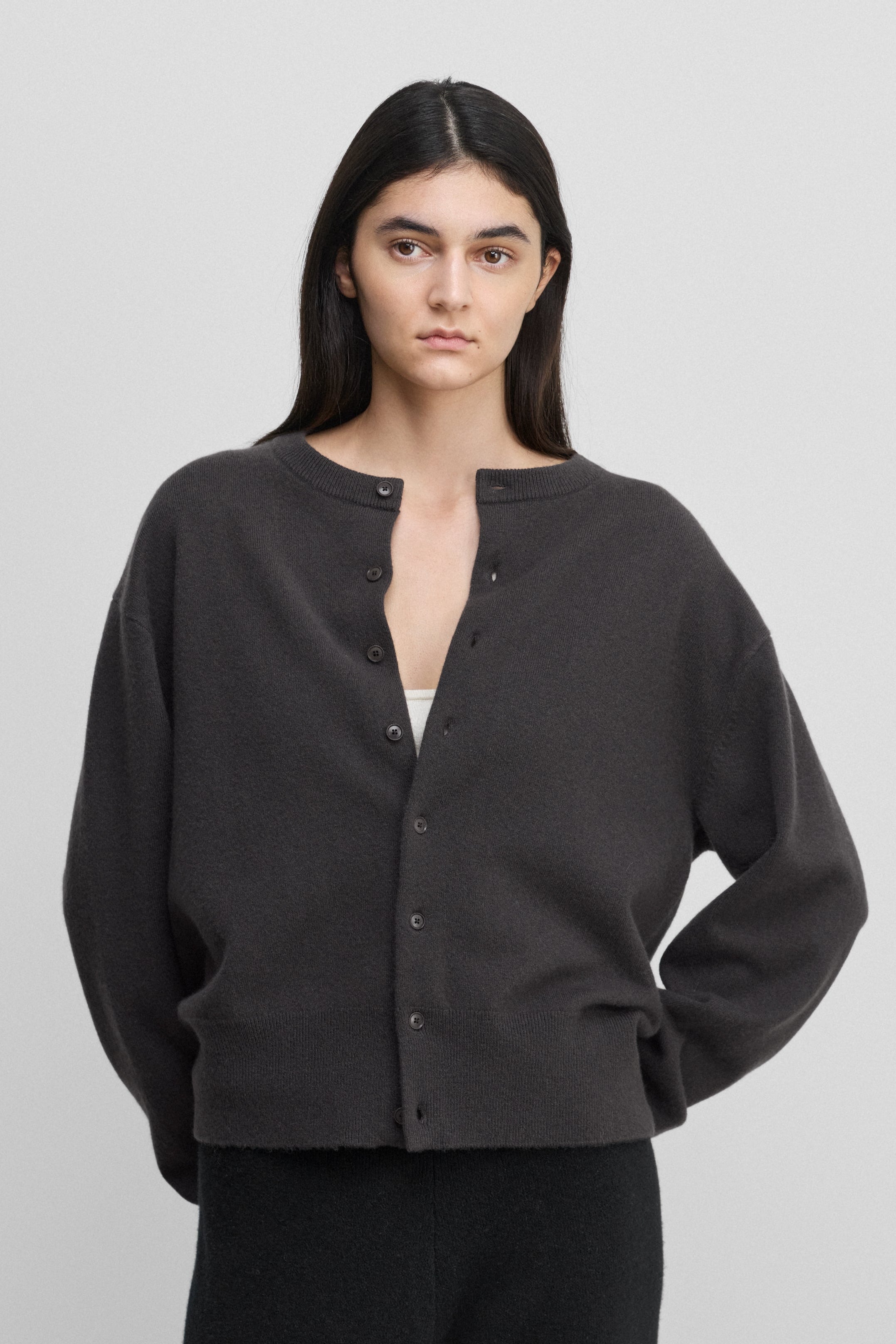 woman wearing a dark grey cashmere crew-neck cardigan with eight corozo buttons and ribbed trims.
