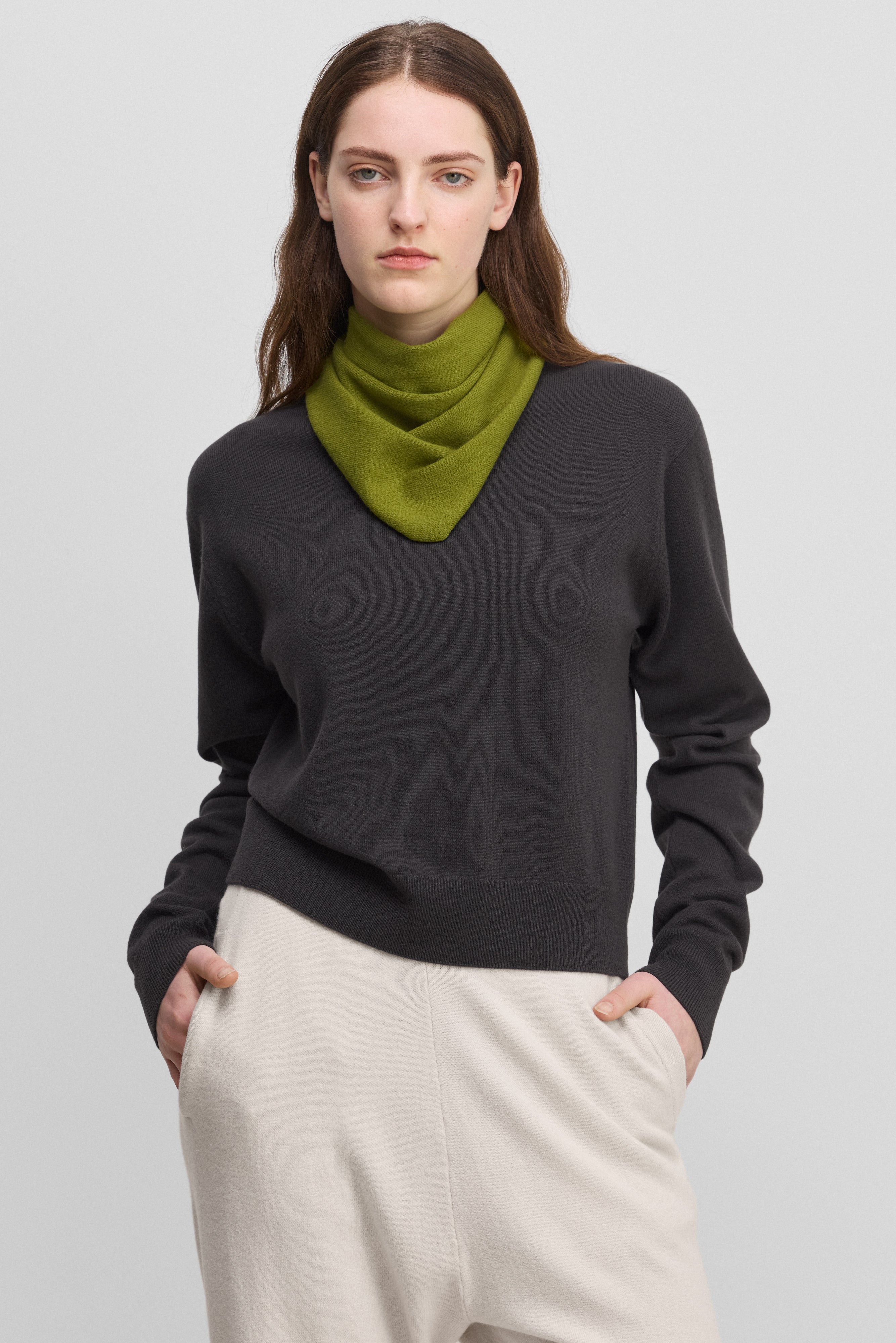 woman wearing a dark grey cashmere crew-neck sweater with ribbed hem, cuffs, neckline, styled with a green scarf.