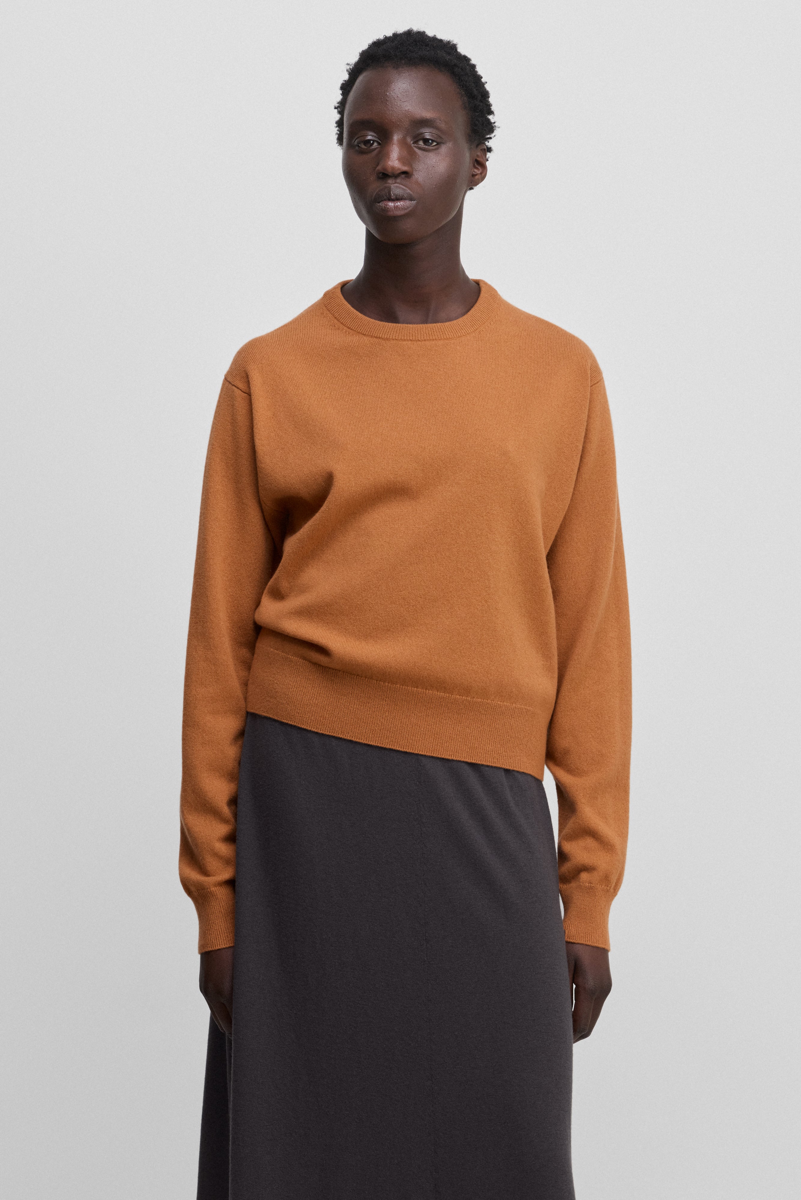 woman wearing an orange cashmere crew-neck sweater with ribbed hem, cuffs, neckline.