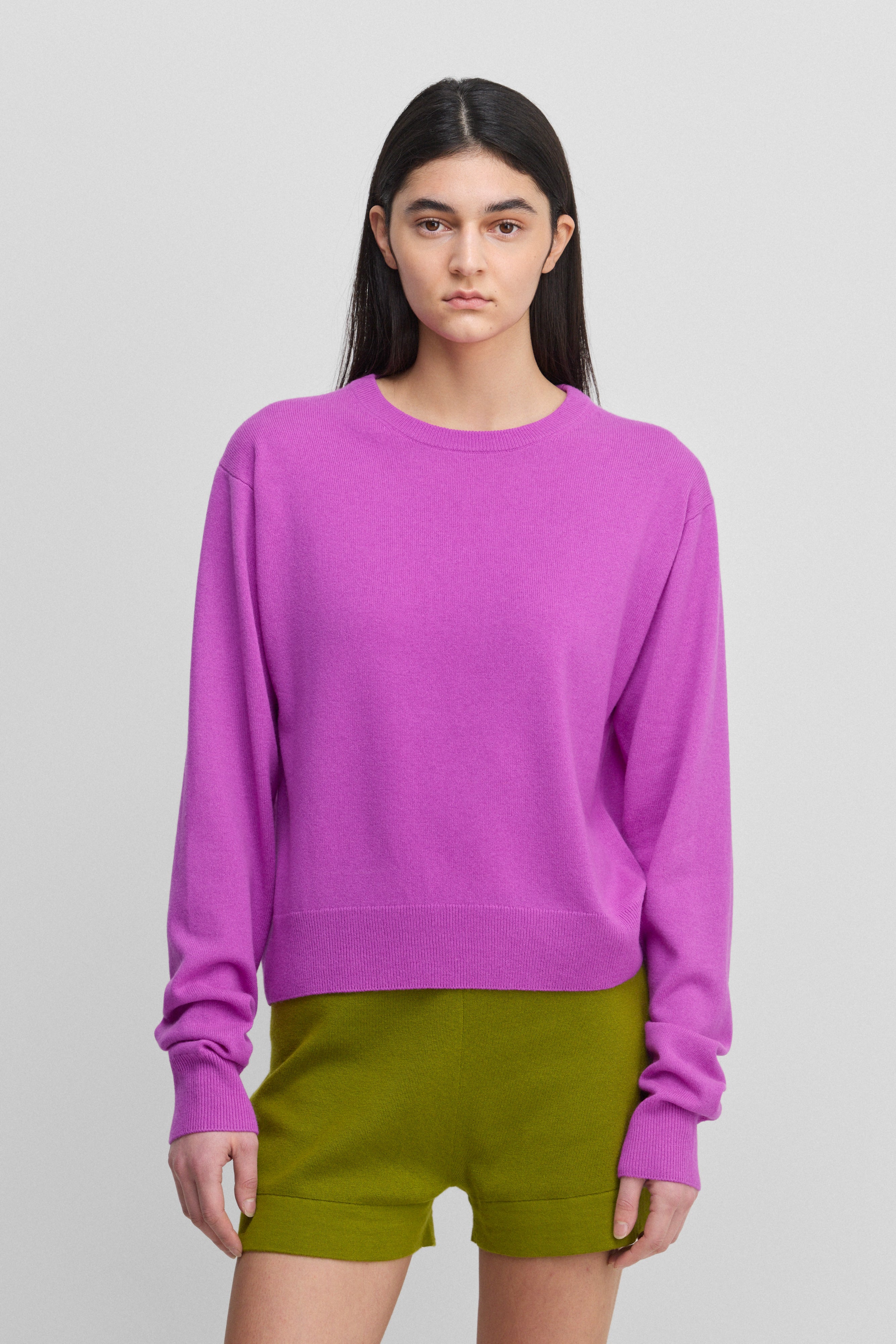 woman wearing a bright pink cashmere crew-neck sweater with ribbed hem, cuffs, neckline.