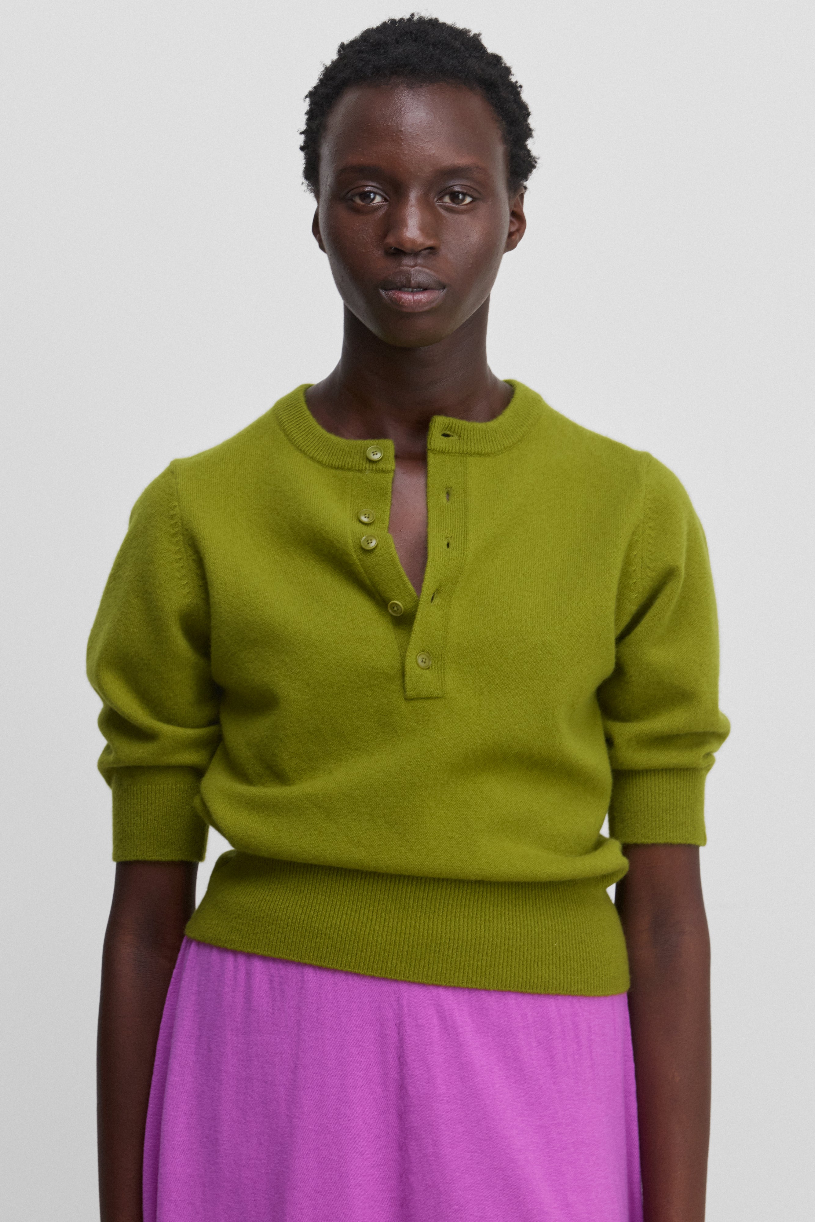 woman wearing a green half-button cashmere sweater with elbow-length sleeves and ribbed trims.