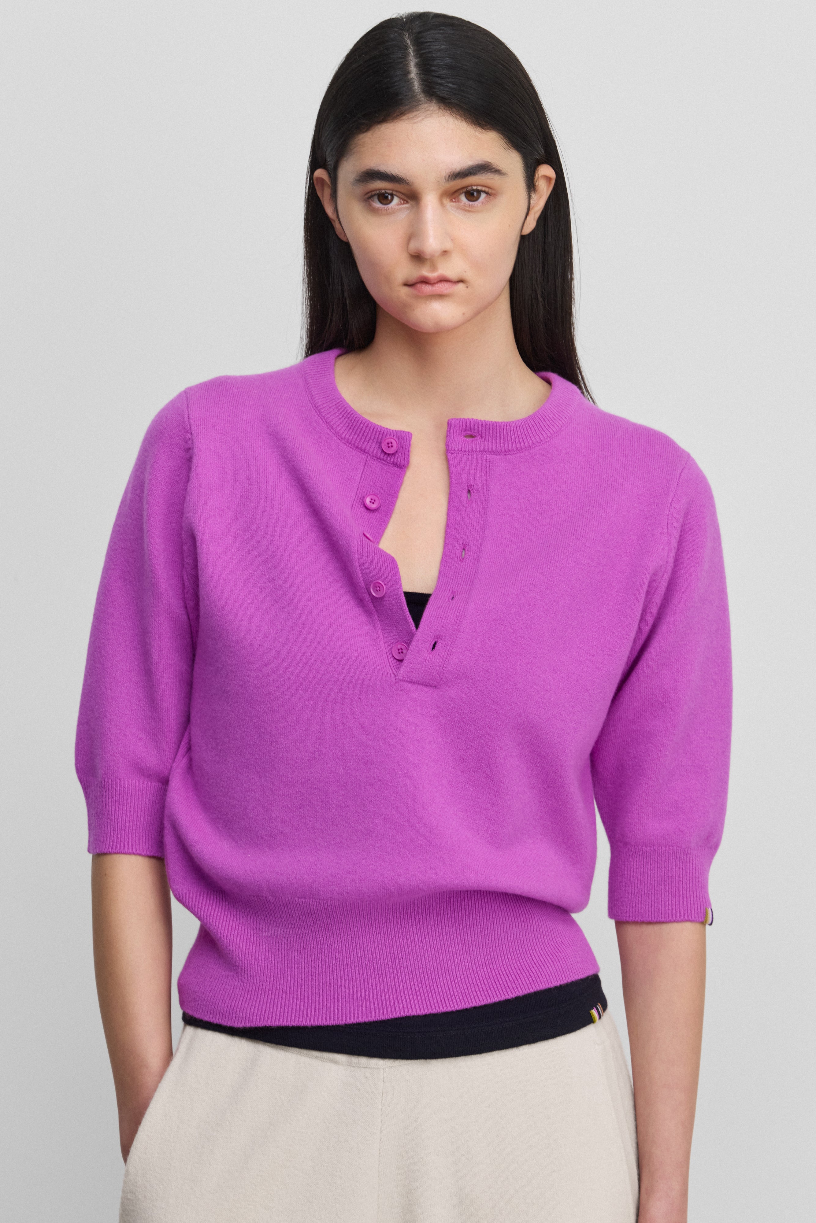 woman wearing a bright pink half-button cashmere sweater with elbow-length sleeves.
