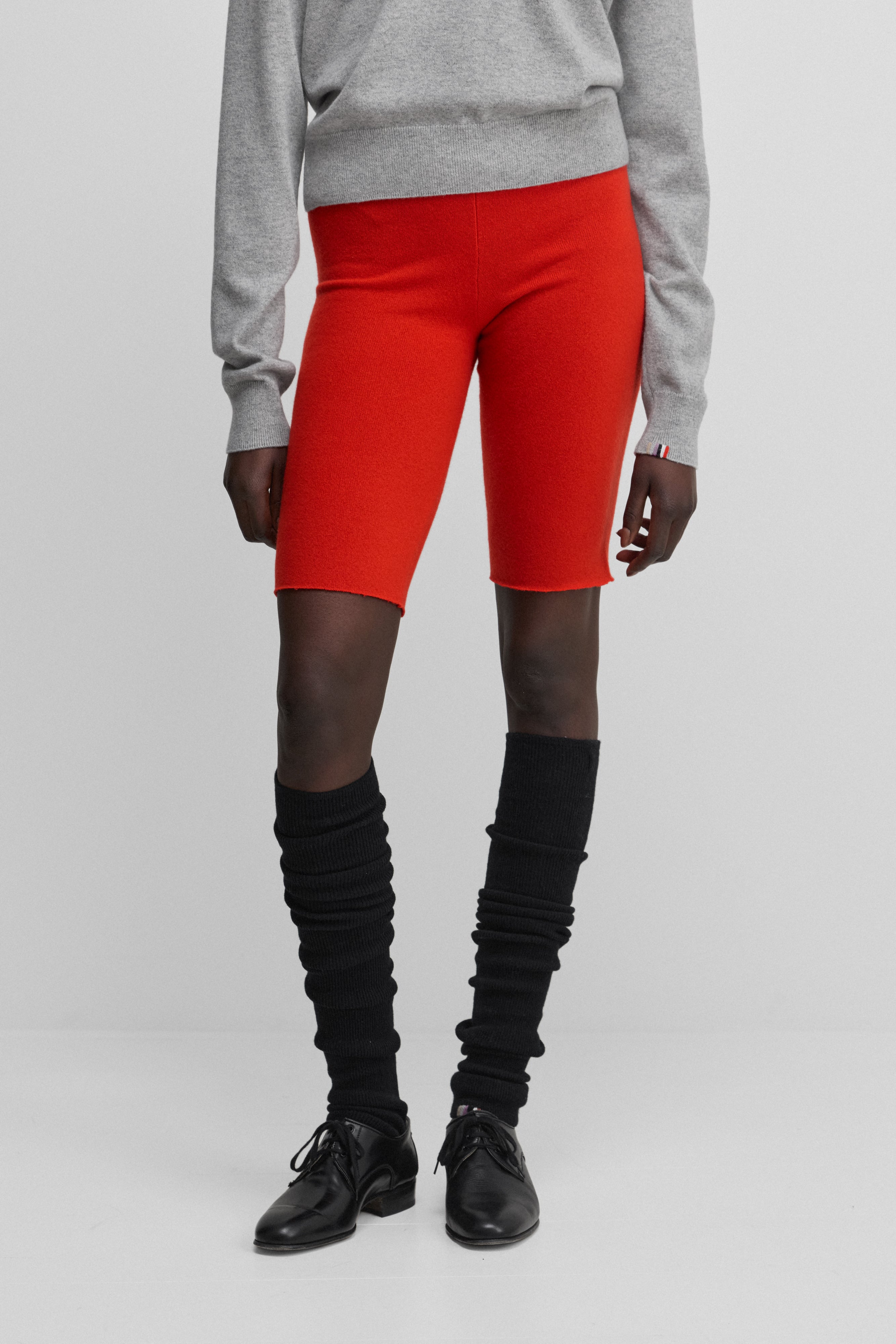 woman wearing black rib-knit cashmere leg warmers, styled with red biker shorts.