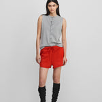 woman wearing a grey sleeveless cotton-cashmere vest with corozo buttons, styled with red shorts.