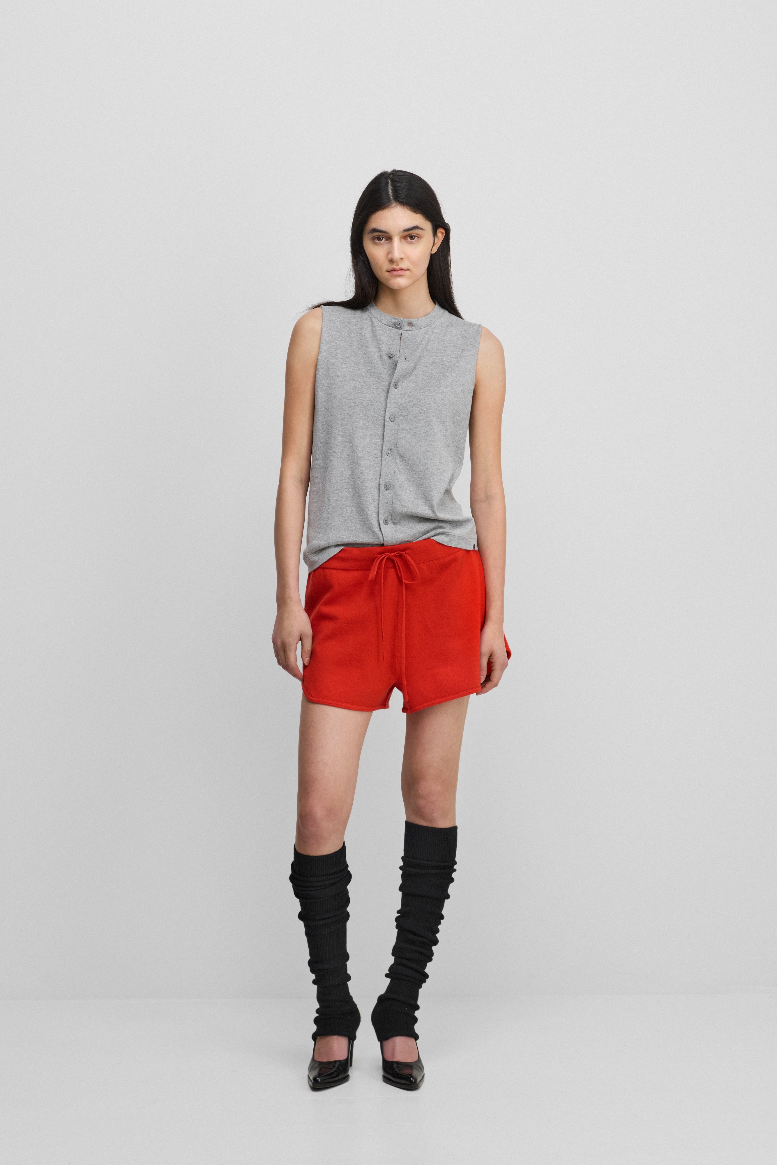woman wearing a grey sleeveless cotton-cashmere vest with corozo buttons, styled with red shorts.