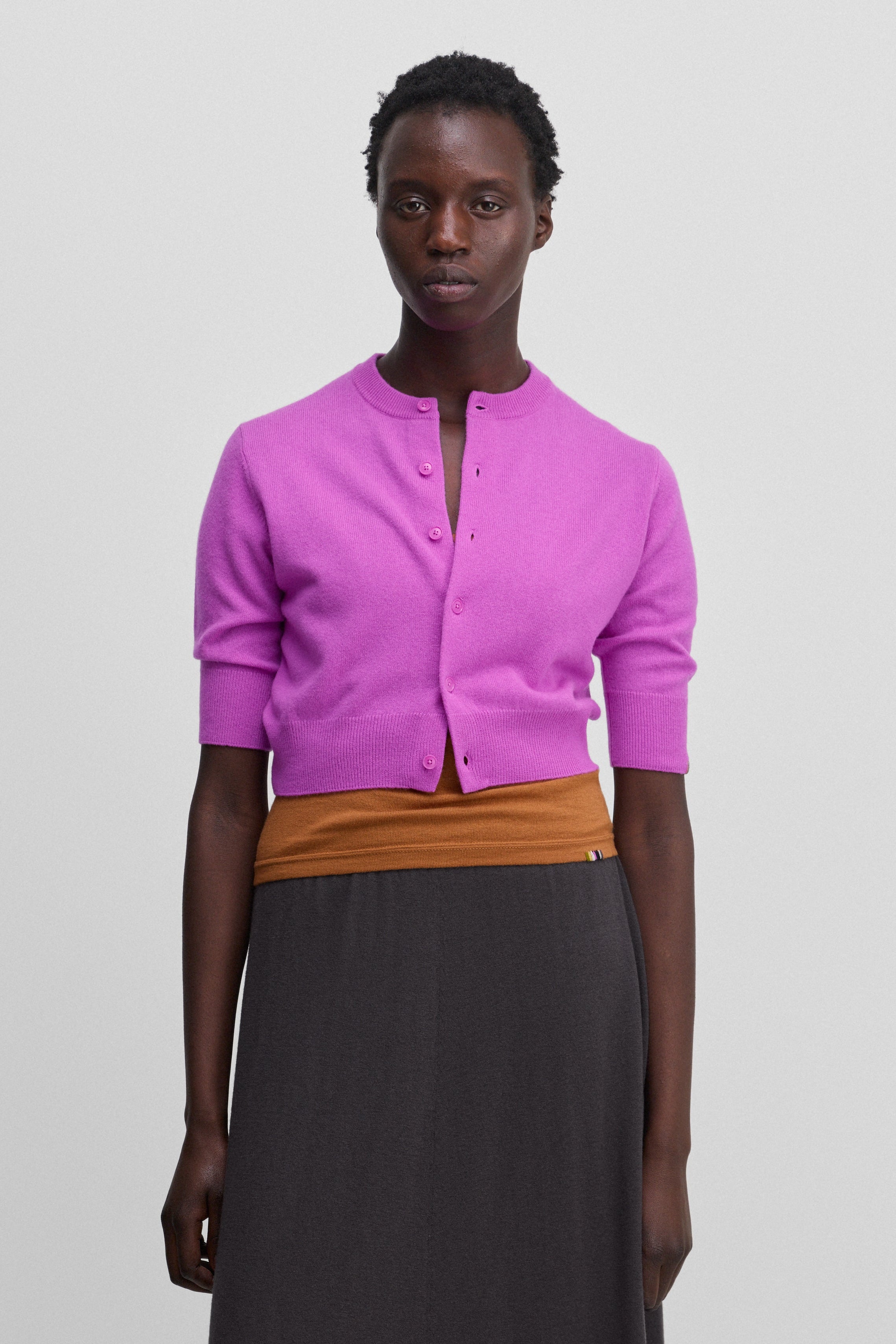 woman wearing a bright pink cropped button-up cardigan with elbow-length sleeves, worn over an orange top.