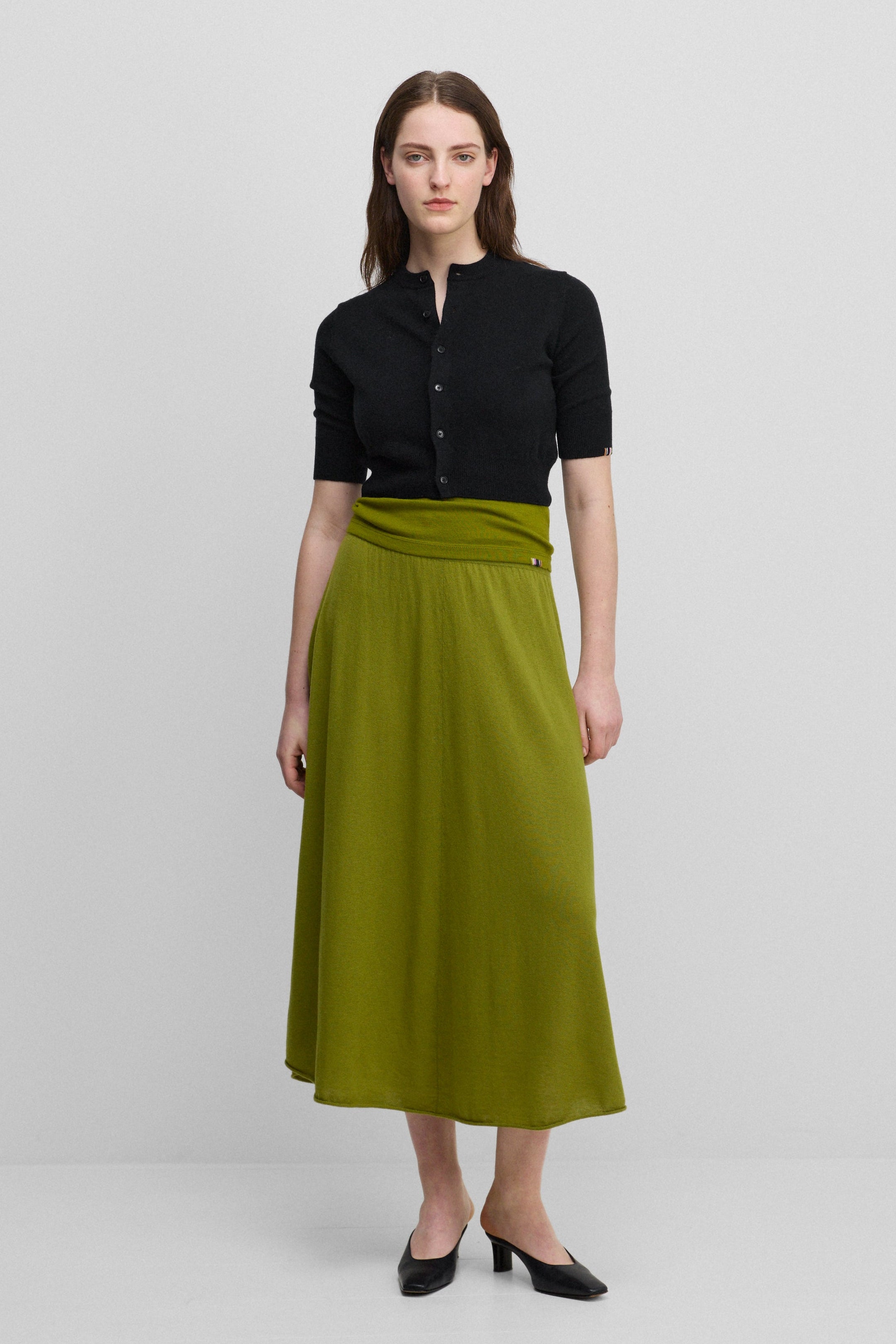 woman wearing a green flared wool cashmere midi skirt, styled with a black cardigan.