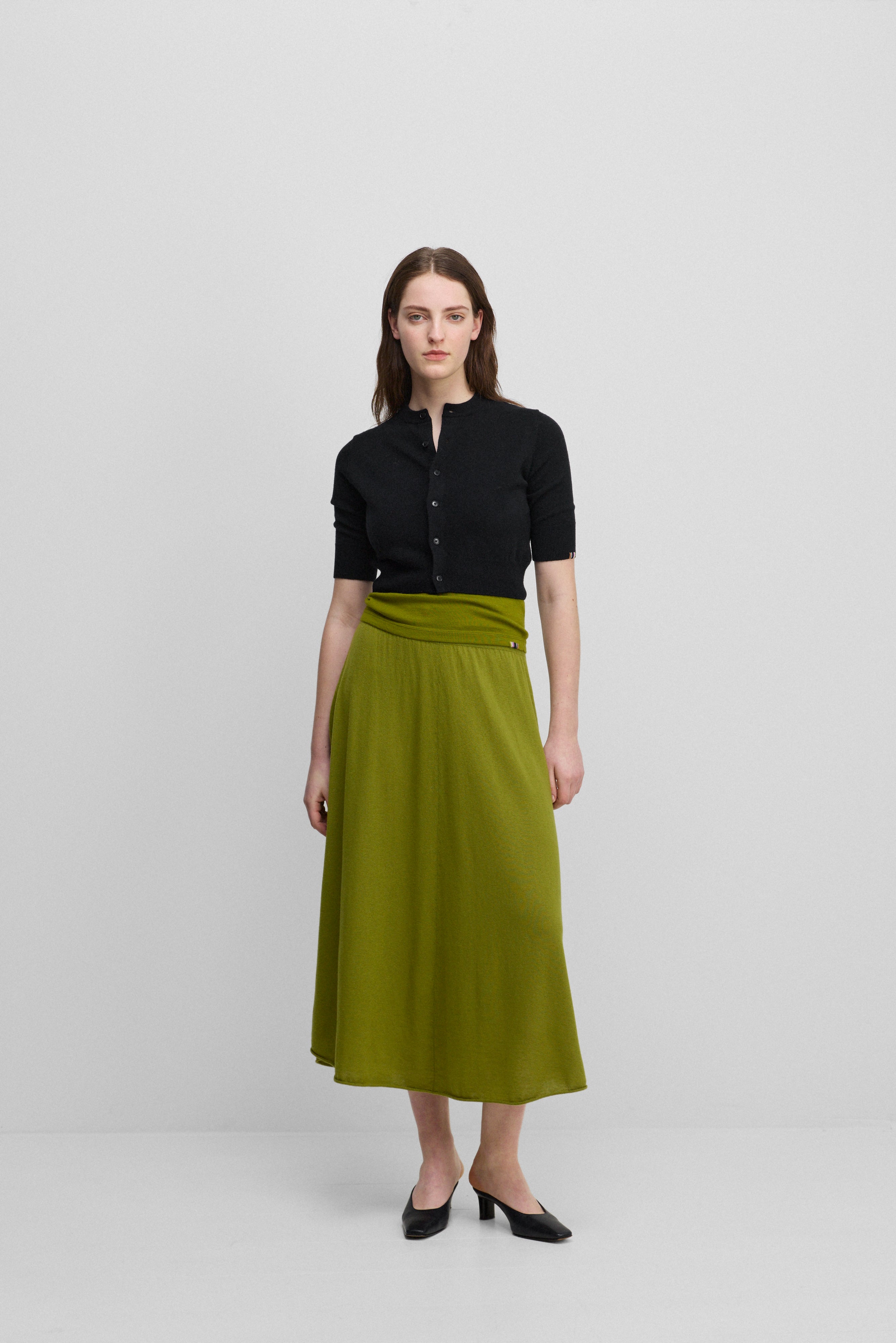 woman wearing a green flared wool cashmere midi skirt, styled with a black cardigan.