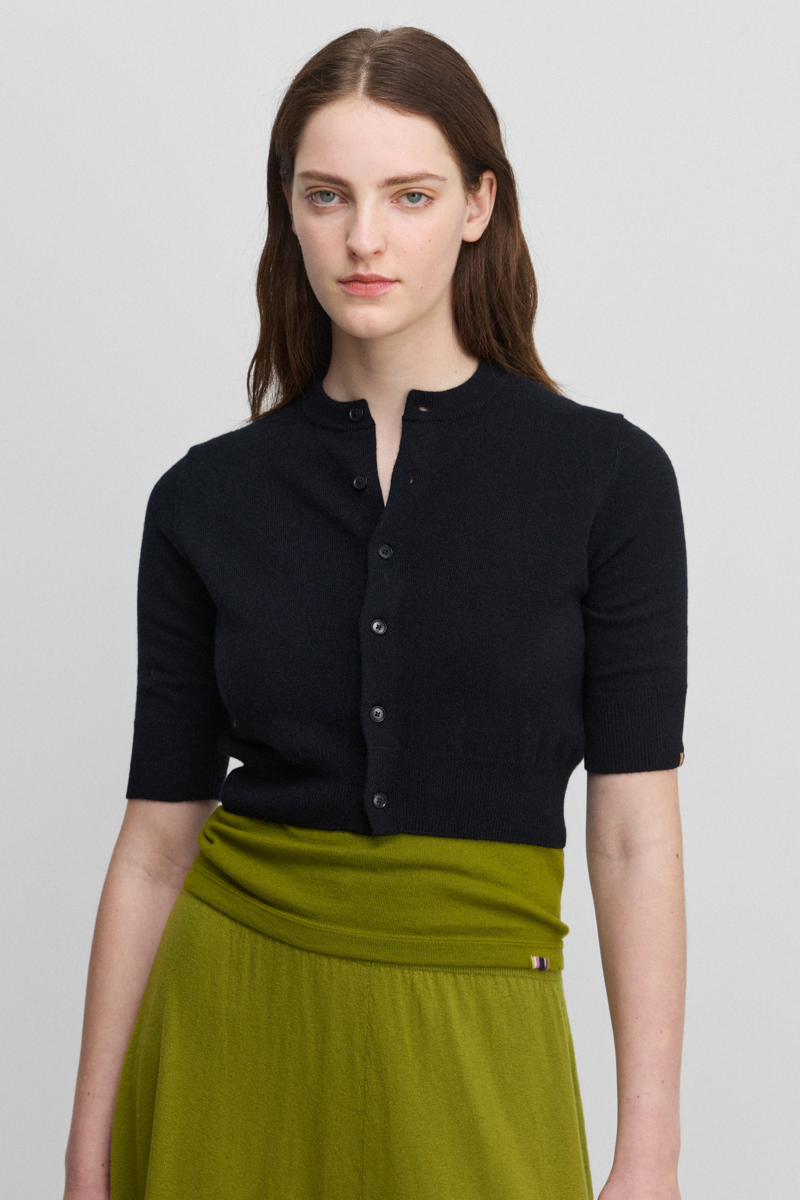 woman wearing a black cropped crew-neck cardigan with six corozo buttons and elbow-length sleeves.