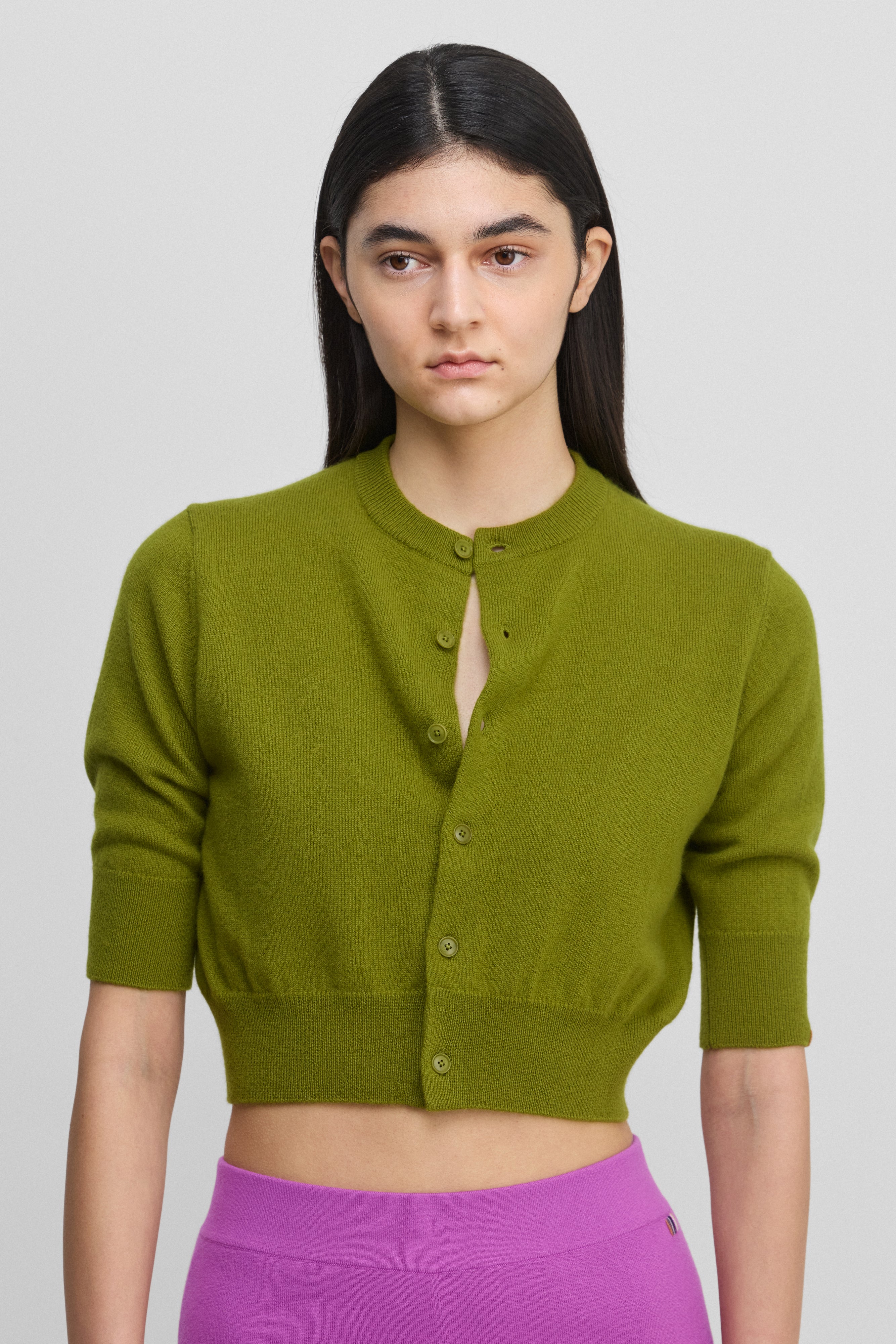 woman wearing a green cropped button-up cardigan with elbow-length sleeves and a crew neck.