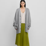 woman wearing a grey oversized chunky cashmere button-up cardigan with pockets, styled with a skirt.